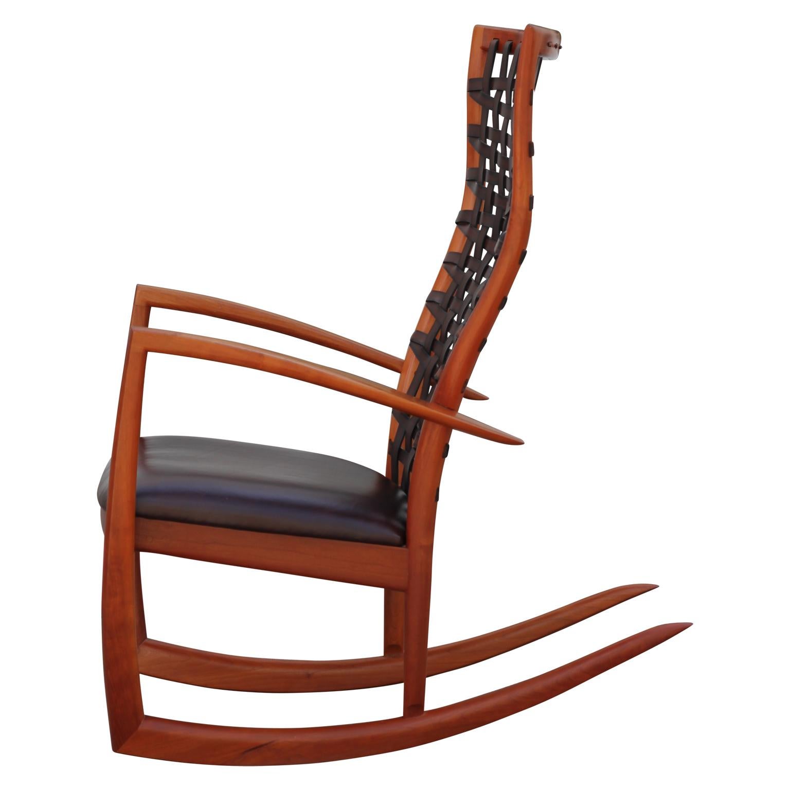 Exquisite handmade rocking chair made from cherrywood with a leather seat and woven leather backing. This sculptural rocking chair has a pair available. The maker, Roger Deatherage is a proudly lives and works in Houston, Texas.