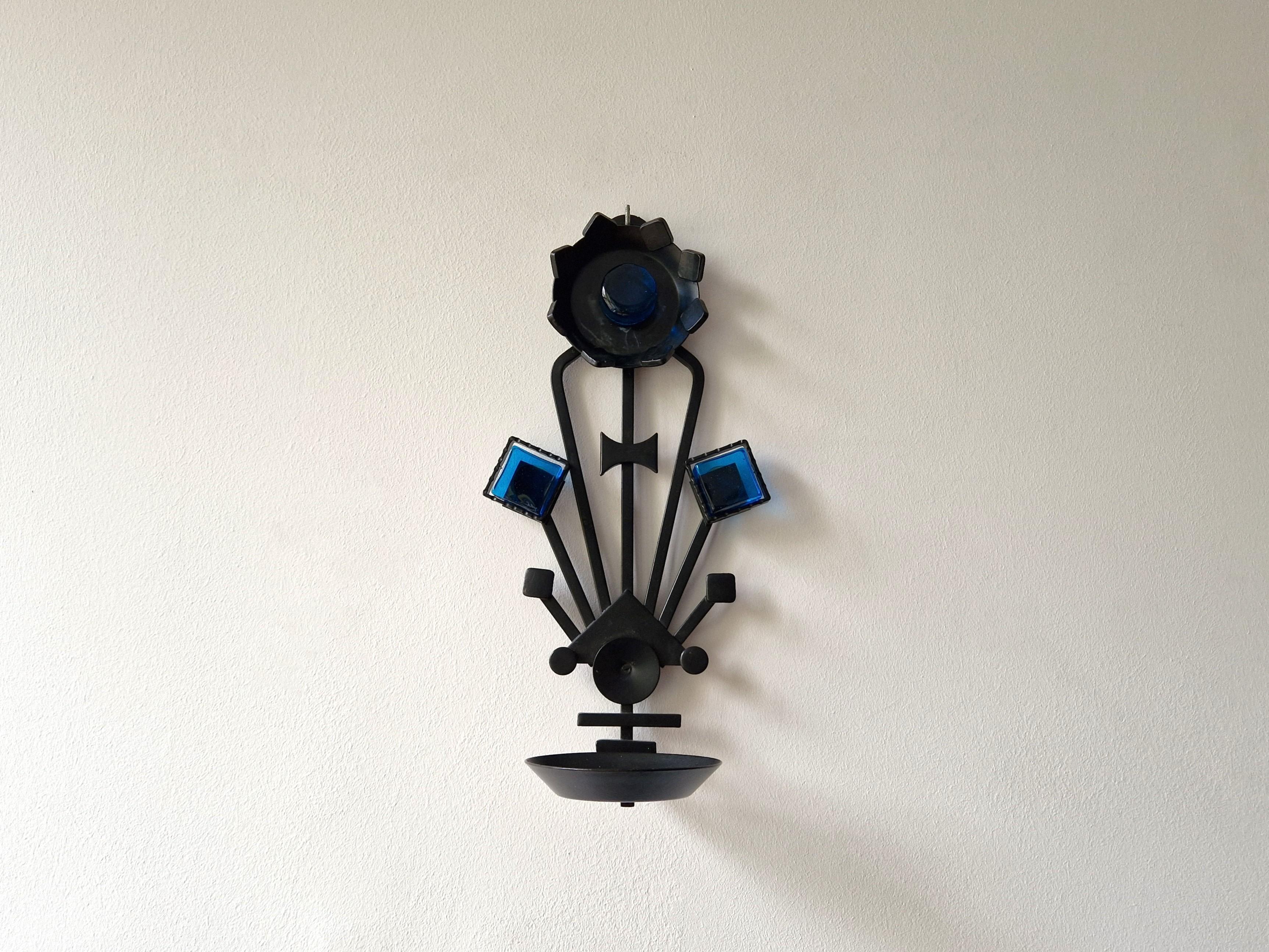 This iron and glass candle candle sconce was made by Dantoft Kunstartikler (art pieces) in Denmark. A stunning piece of wall art of Danish design. It is made out of lacquered wrought iron with beautiful pieces of blue glass. It can hold a pillar