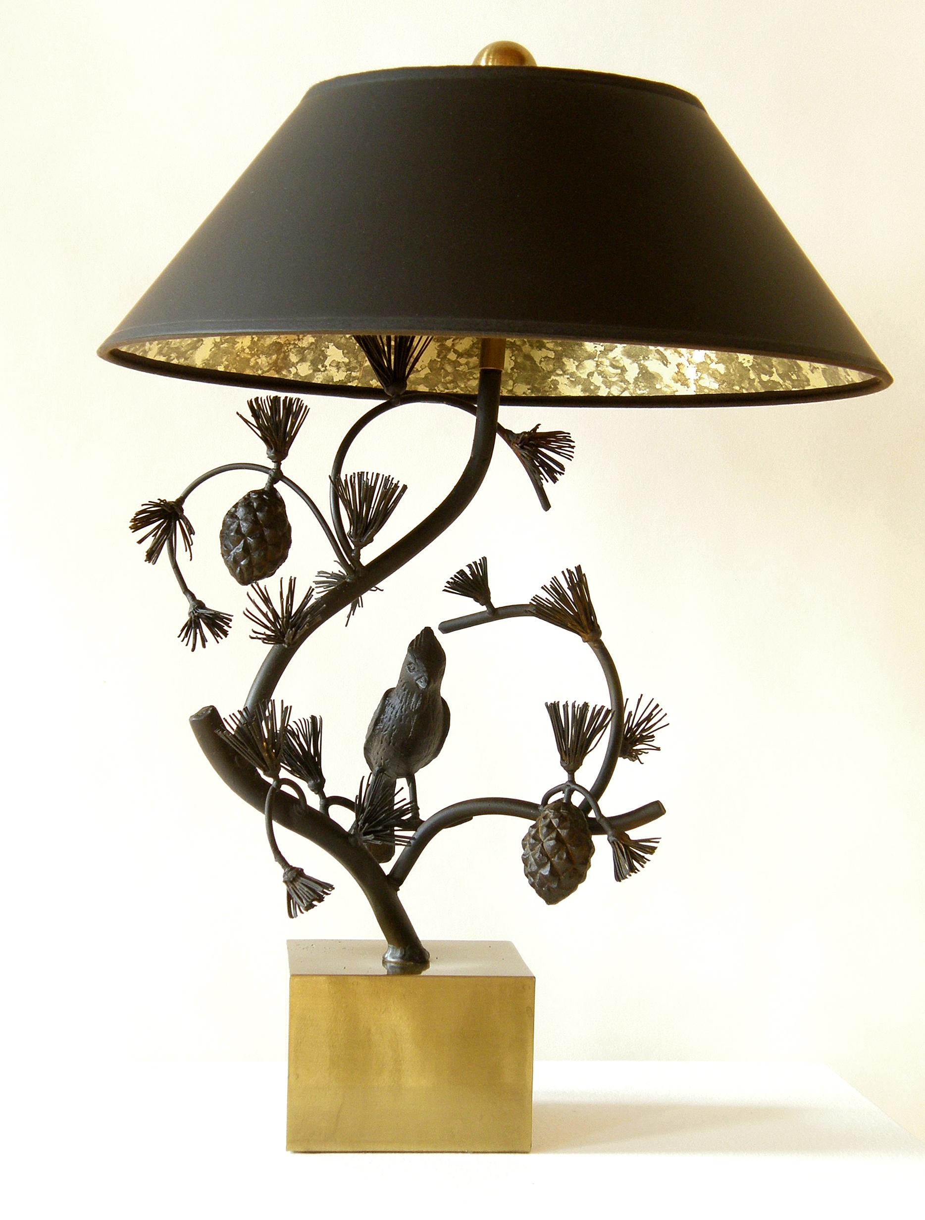 This sweet lamp by Chapman features a sculptural tree form in iron with a cardinal (?) perched on a branch. It has a natural style and pleasant asymmetry. The cube base is brass, and the black shade is lined with gold and black mottled paper. The