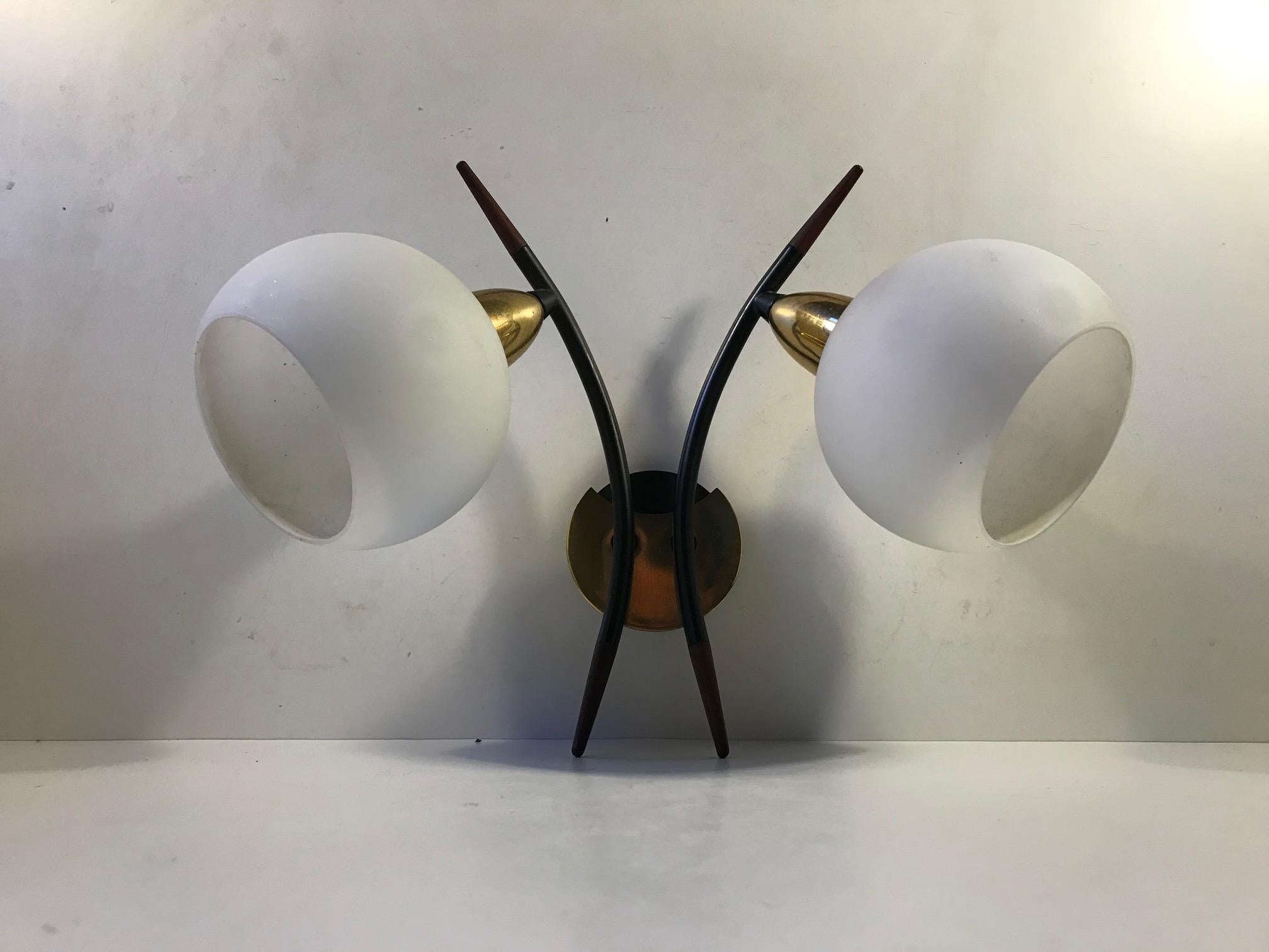 Twin sconce designed in a style reminiscent of Stilnovo and manufactured in the 1950s by anonymous Italian maker or designer. It is made from brass, black powder-coated steel and matte white opaline glass. The teak accents to the arching black arms