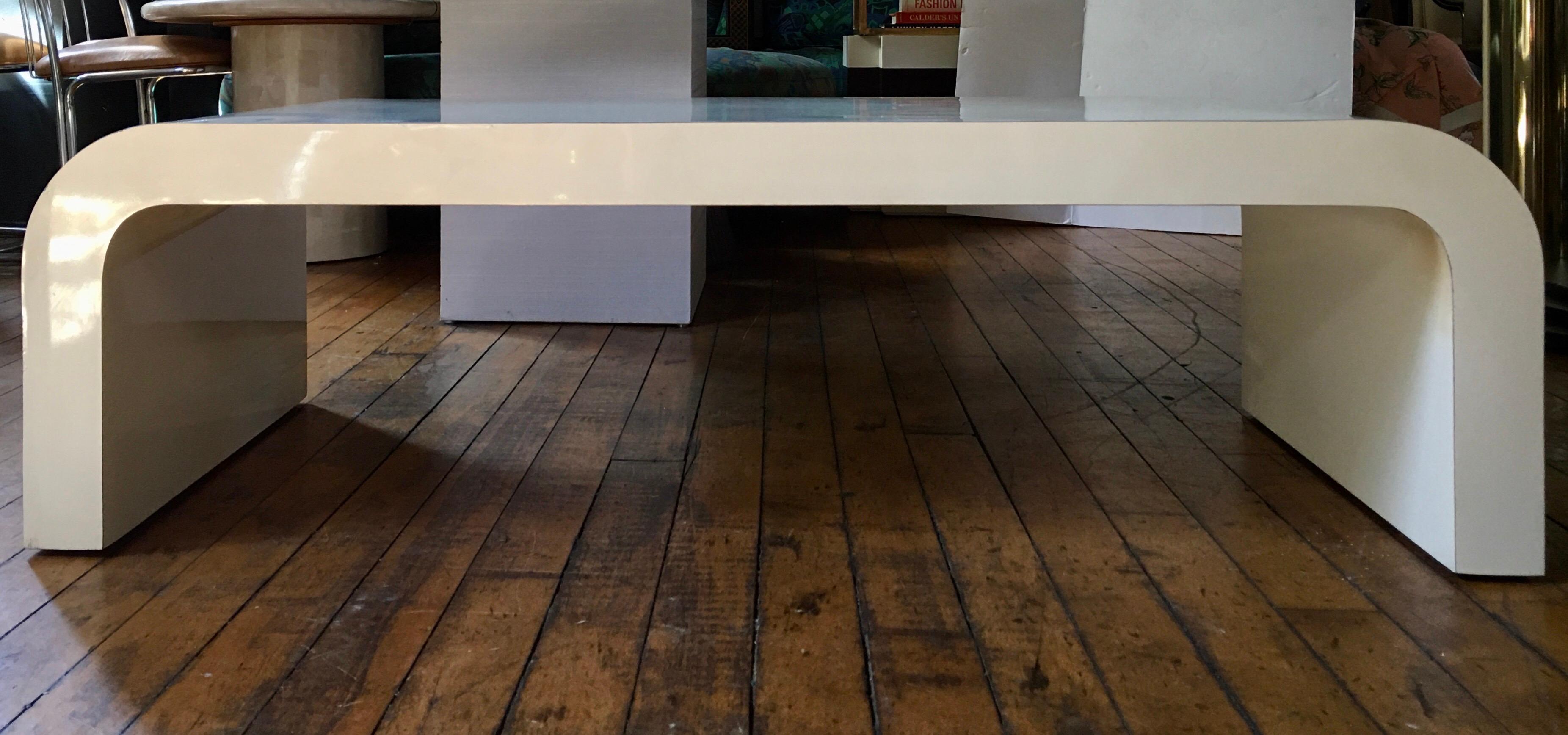 1980s sculptural curved waterfall wood coffee table covered in a neutral beige tone gloss laminate. In the style of Karl Springer.