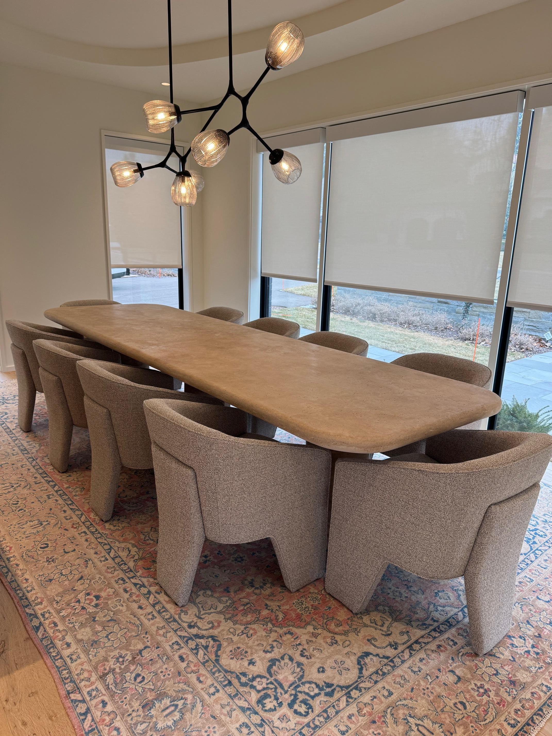 This table is a functional work of art that elevates any space with its organic, modern, minimalist design. Crafted from honed travertine, it features a substantial two piece tabletop with elegantly curved edges, resting gracefully on three
