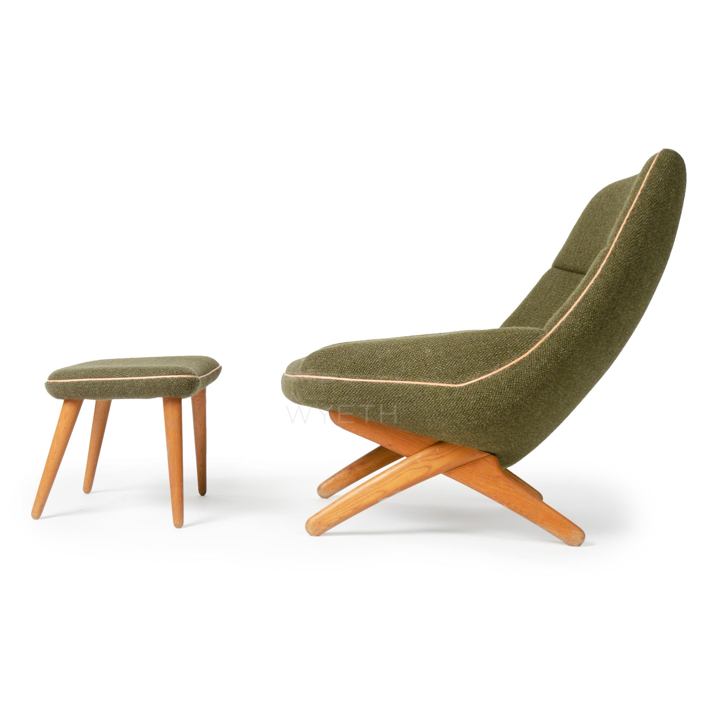 A sculptural upholstered lounge chair having crossed legs and an accompanying ottoman with turned-dowel legs in green upholstery with natural leather piping.
