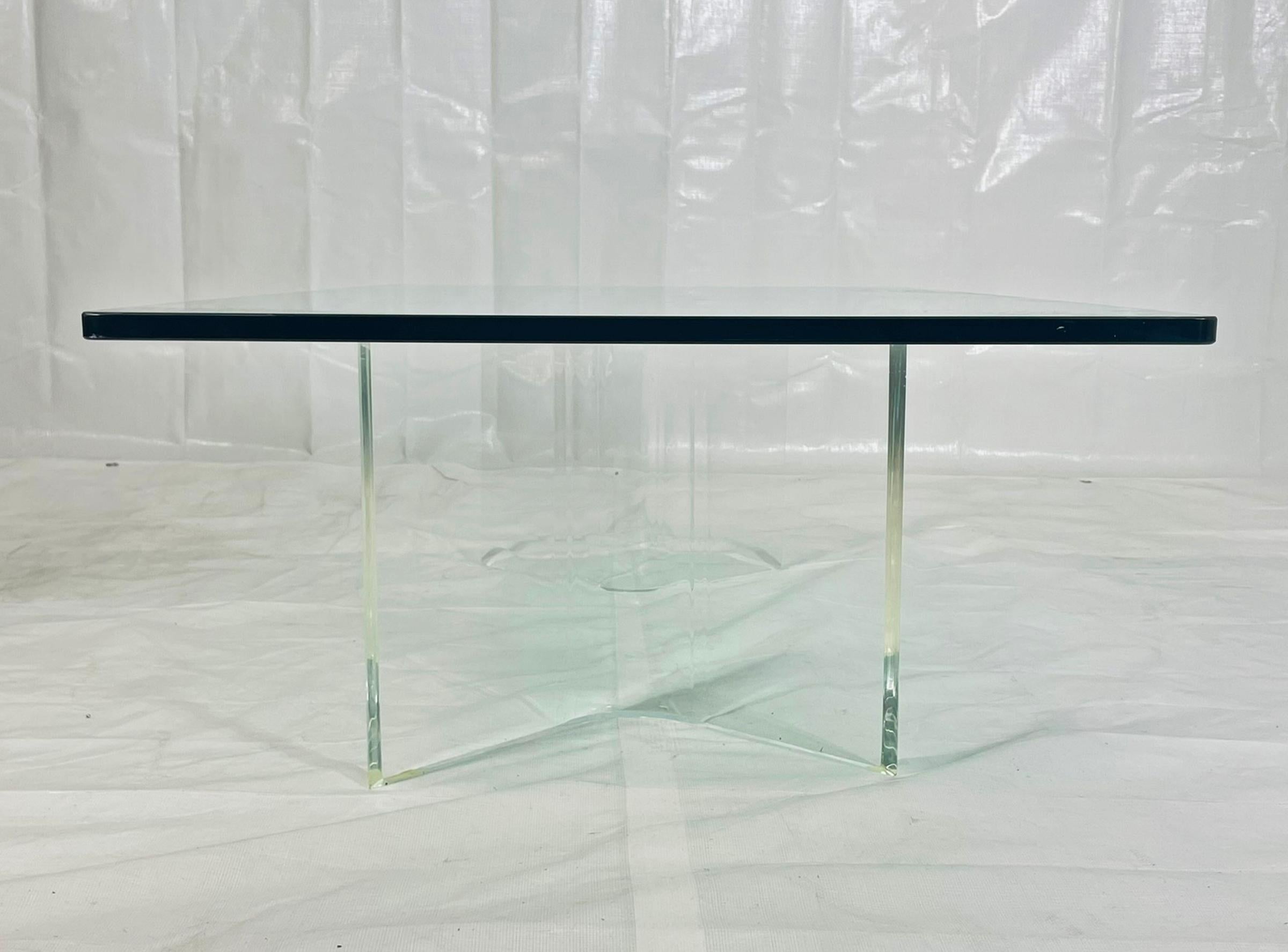 Table basse américaine vintage des années 1980 en Lucite, composée de deux bases sculpturales en Lucite clair et d'un épais plateau rectangulaire en verre. Les bases sont formées de Lucite de gros calibre façonné en plans angulaires nets, donnant à