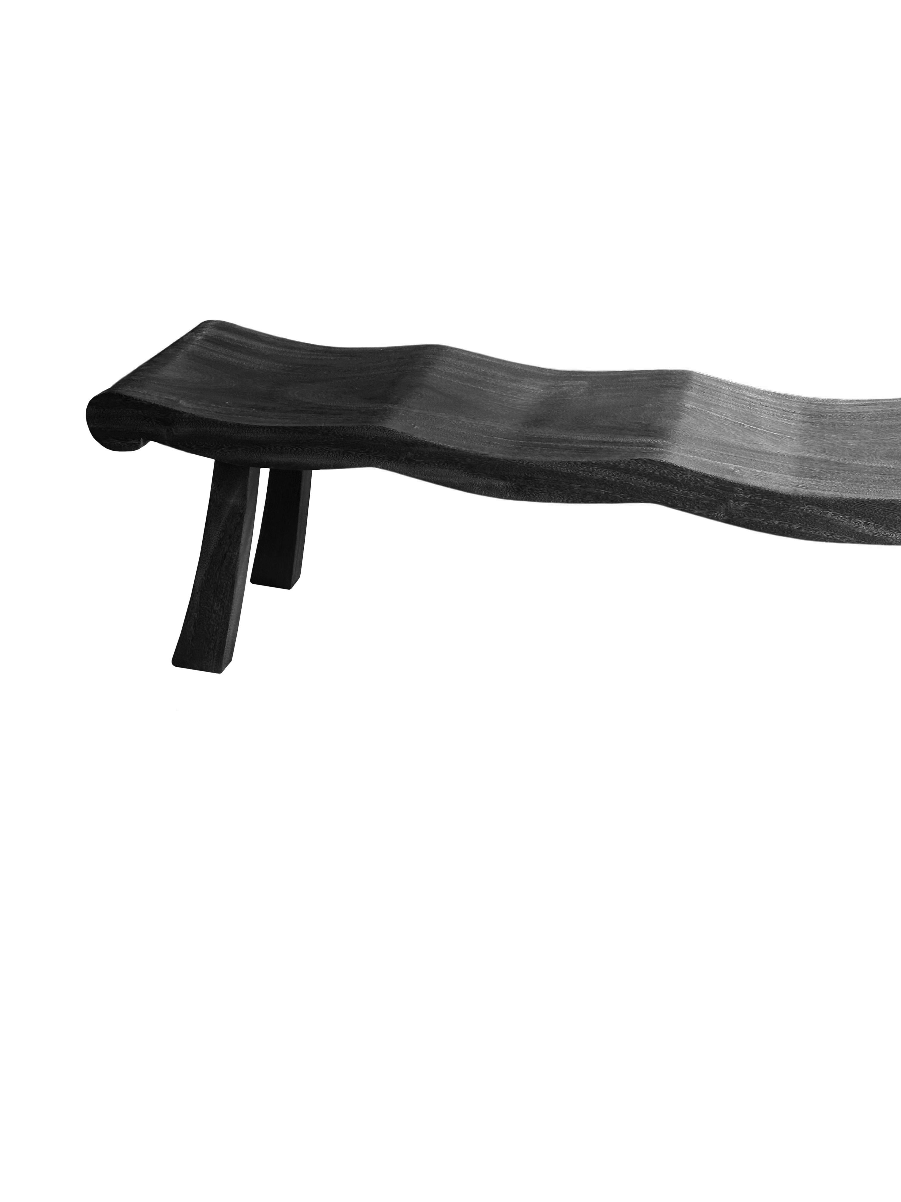 Un banco de madera de mango maravillosamente escultural con un acabado quemado. Para conseguir su pigmentación, la madera se quemó varias veces y se terminó con una capa transparente. La mezcla de líneas curvas y rectas le añade encanto. El banco se