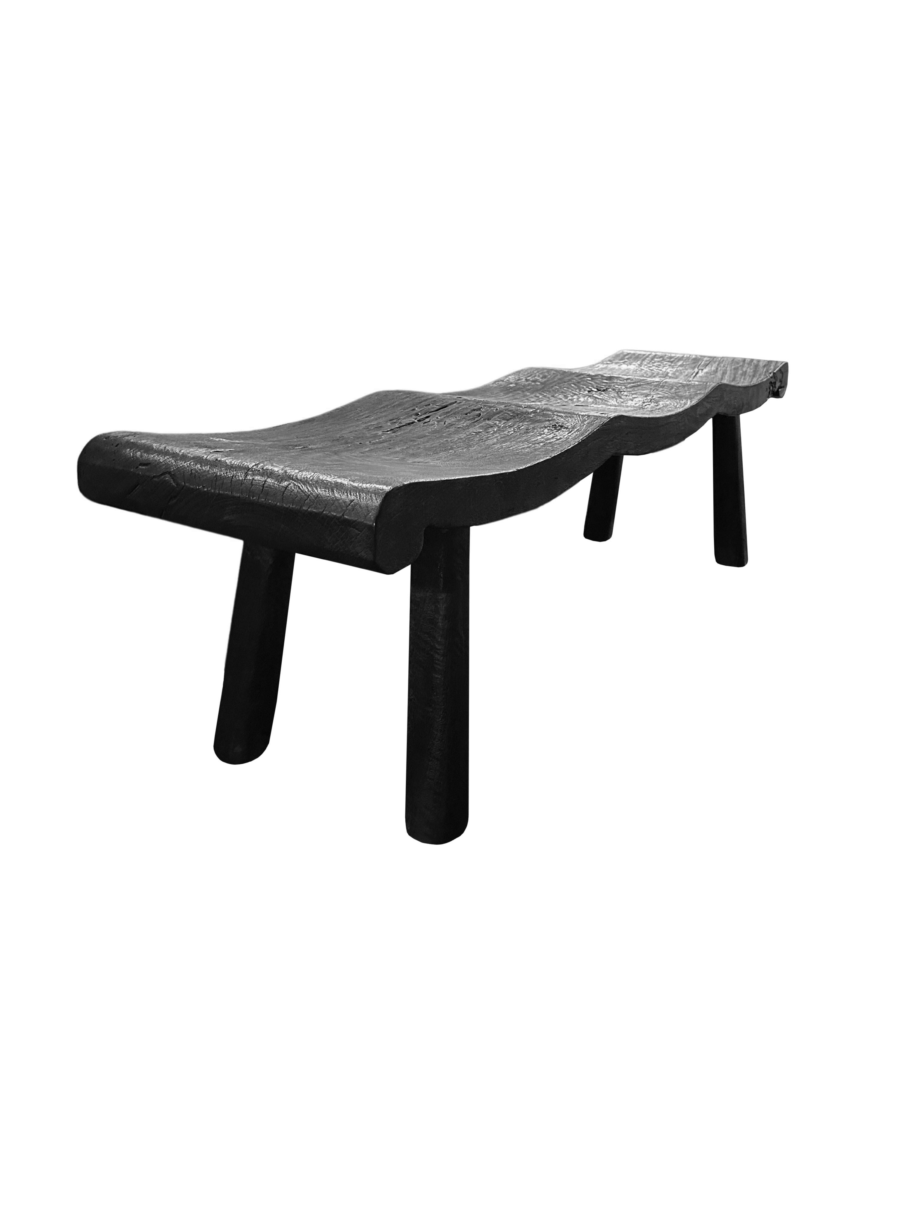 Un banco de madera de mango maravillosamente escultural con un acabado quemado. Para conseguir su pigmentación, la madera se quemó varias veces y se terminó con una capa transparente. La mezcla de líneas curvas y rectas le añade encanto. El banco se