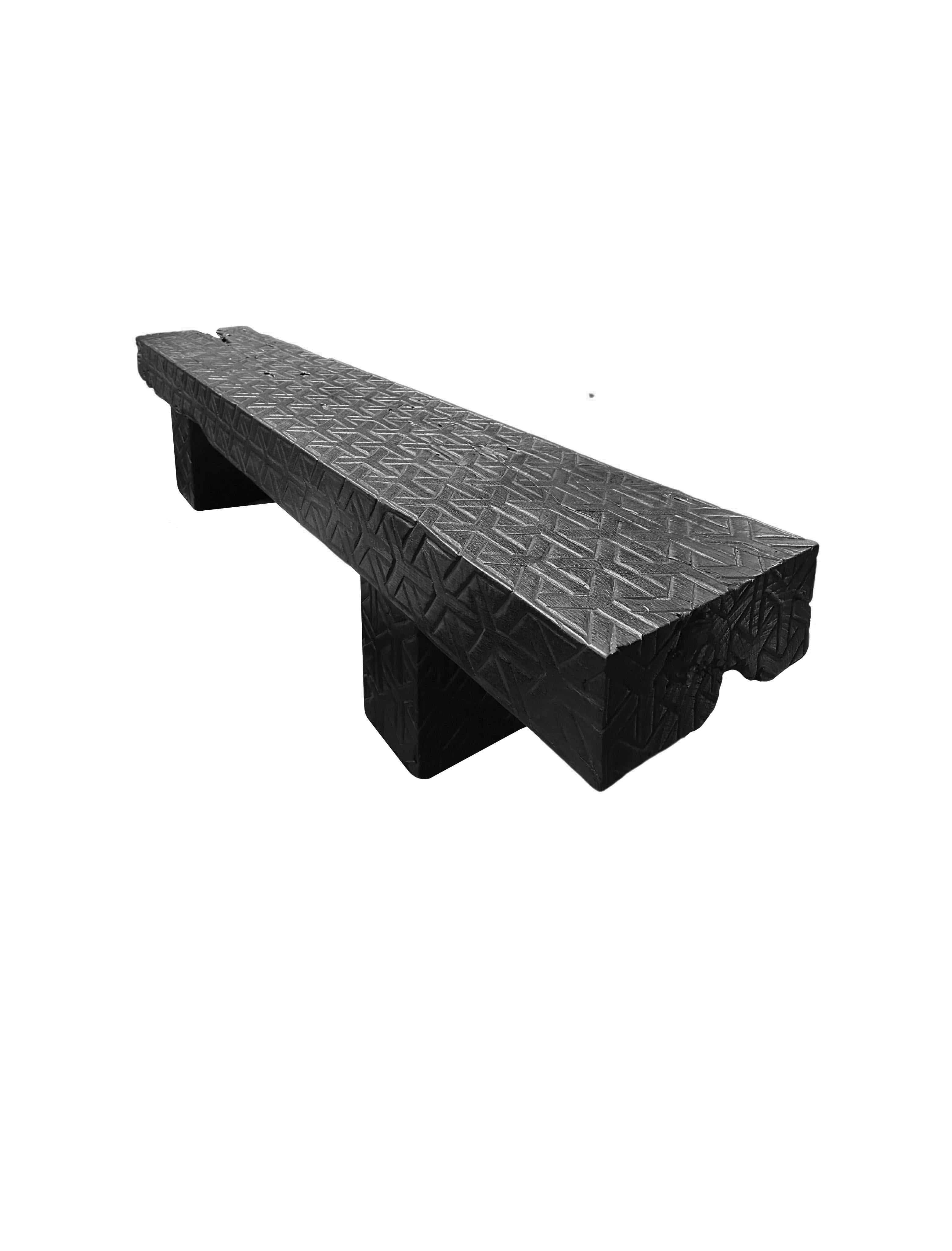 A sculptural hand-carved mango wood bench. To achieve is rich black pigment the bench was burnt three times and then finished with a clear coat. Unique to this bench is the hand carved detailing present on all sides. This carved dealing is meant to