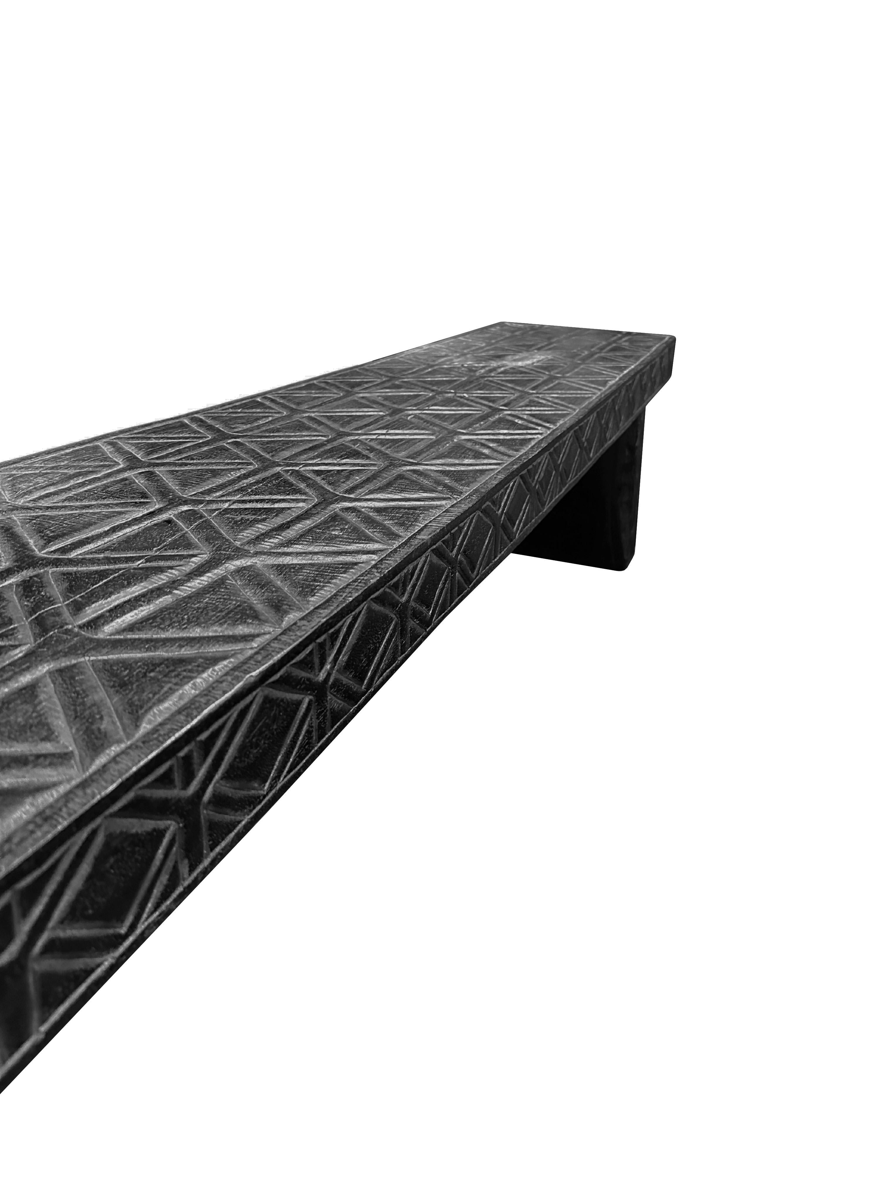 A sculptural hand-carved mango wood bench. To achieve is rich black pigment the bench was burnt three times and then finished with a clear coat. Unique to this bench is the hand carved detailing present on all sides. This carved dealing is meant to
