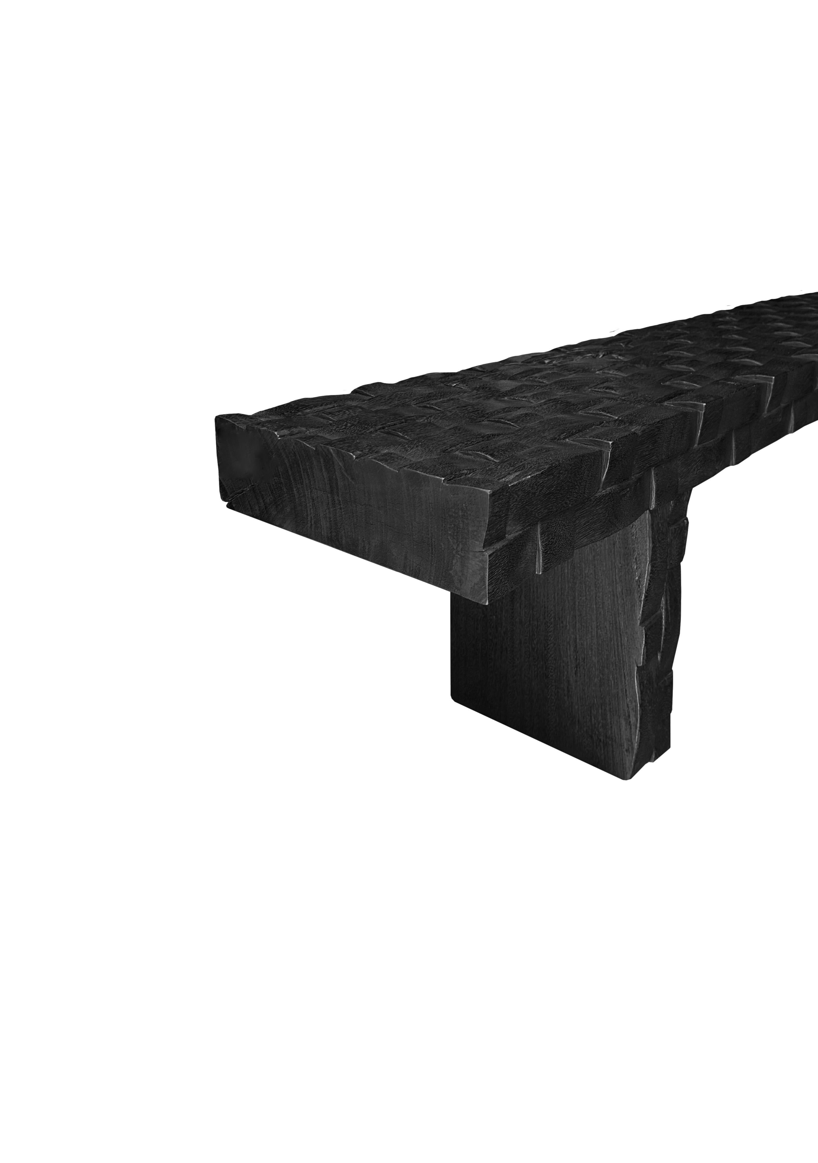 A sculptural hand-carved mango wood bench. To achieve is rich black pigment the bench was burnt three times and then finished with a clear coat. The mix of curved and straight lines along with a myriad of textures make for a very elegant bench.