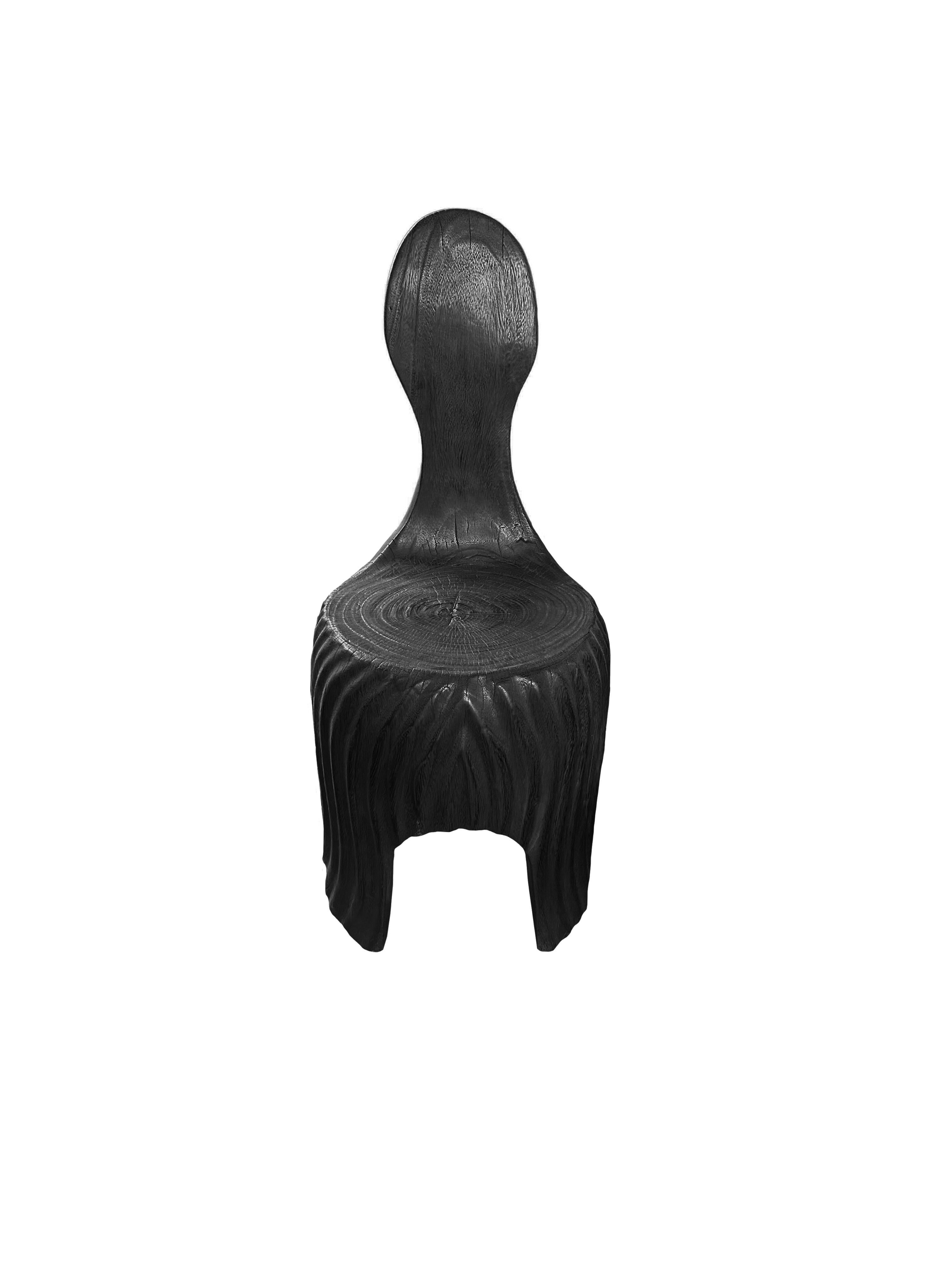 This exquisite sculptural chair, crafted from mango wood, features a striking burnt black finish that enhances its natural grain and texture. The chair’s design showcases elegant, subtle curves that flow seamlessly into a beautifully carved