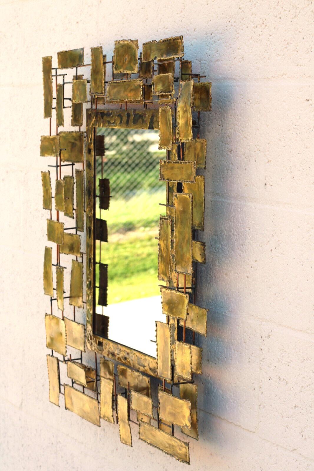 Mid-century Modern sculptural Brutalist wall mirror. Designed in the manner of Curtis Jere. Made of patinated brass/metal, ready to hang. The design around the mirror features a grid work of beaded rough-cut rectangles. Light glitters from the