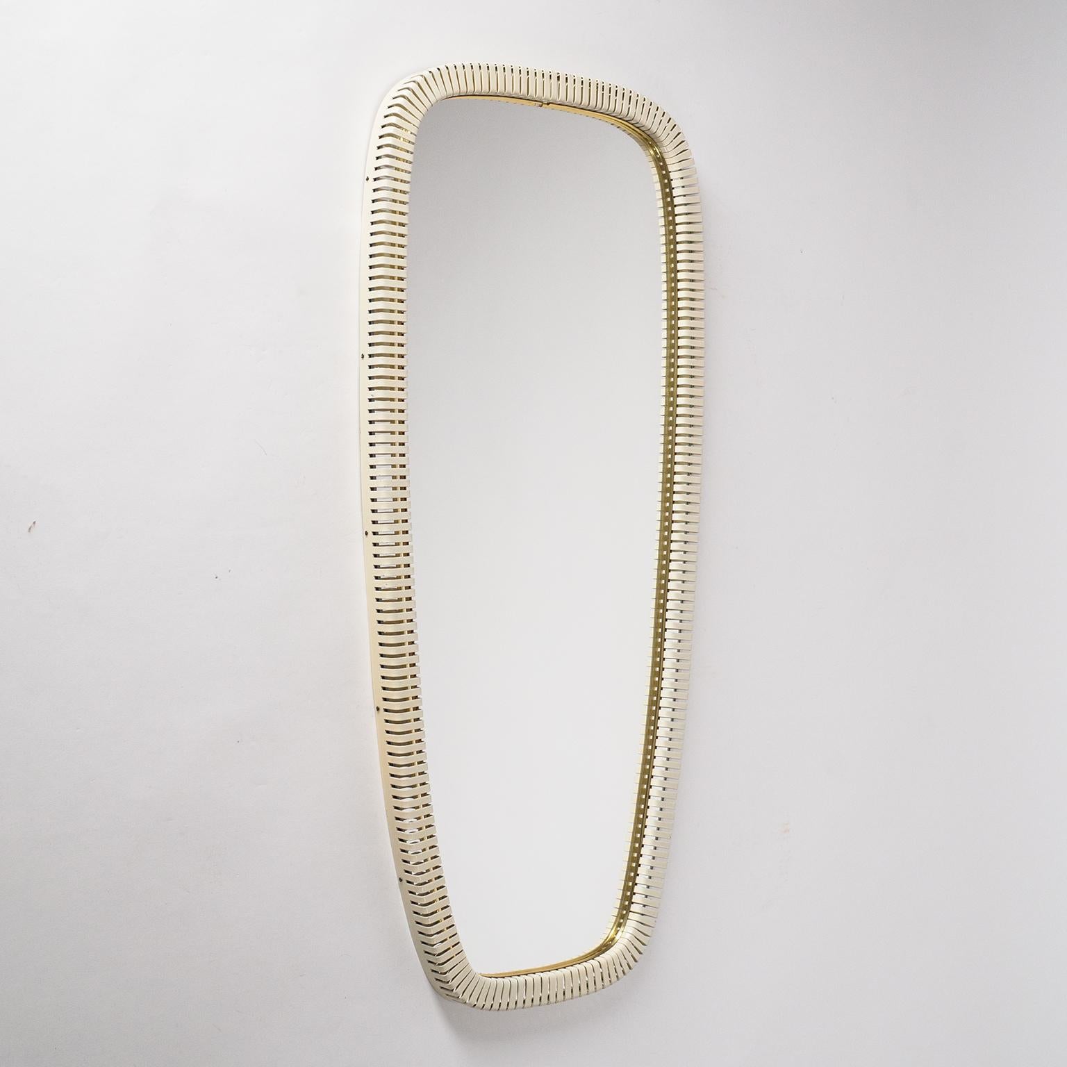 Very unique slender wall mirror, circa 1960, by Vereinigte Werkstätten, Germany. The seamless border of this mirror is made of off-white lacquered profiled steel with periodic incisions or slits and a brass inner rim. Since the reflective area