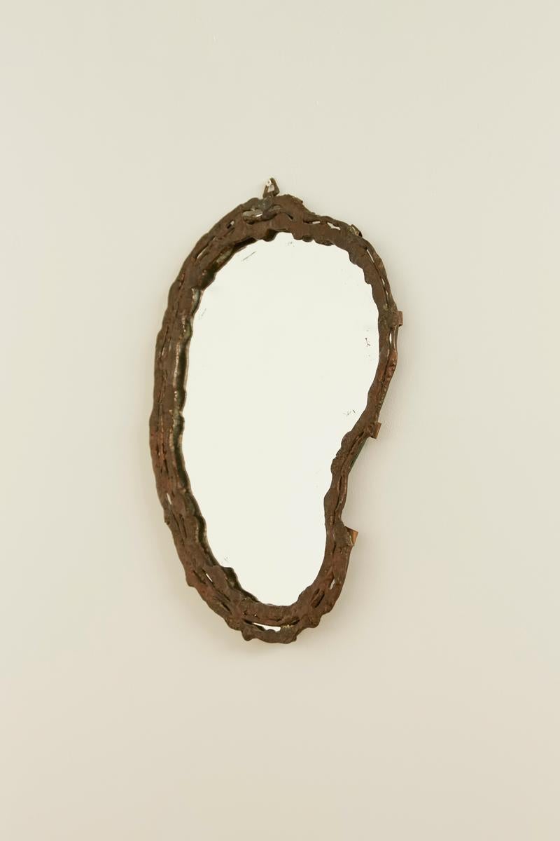 Uno specchio organico e scultoreo con una cornice irregolare in metallo lavorato a mano. La finitura grezza e strutturata e la forma asimmetrica ne fanno un pezzo di grande effetto.