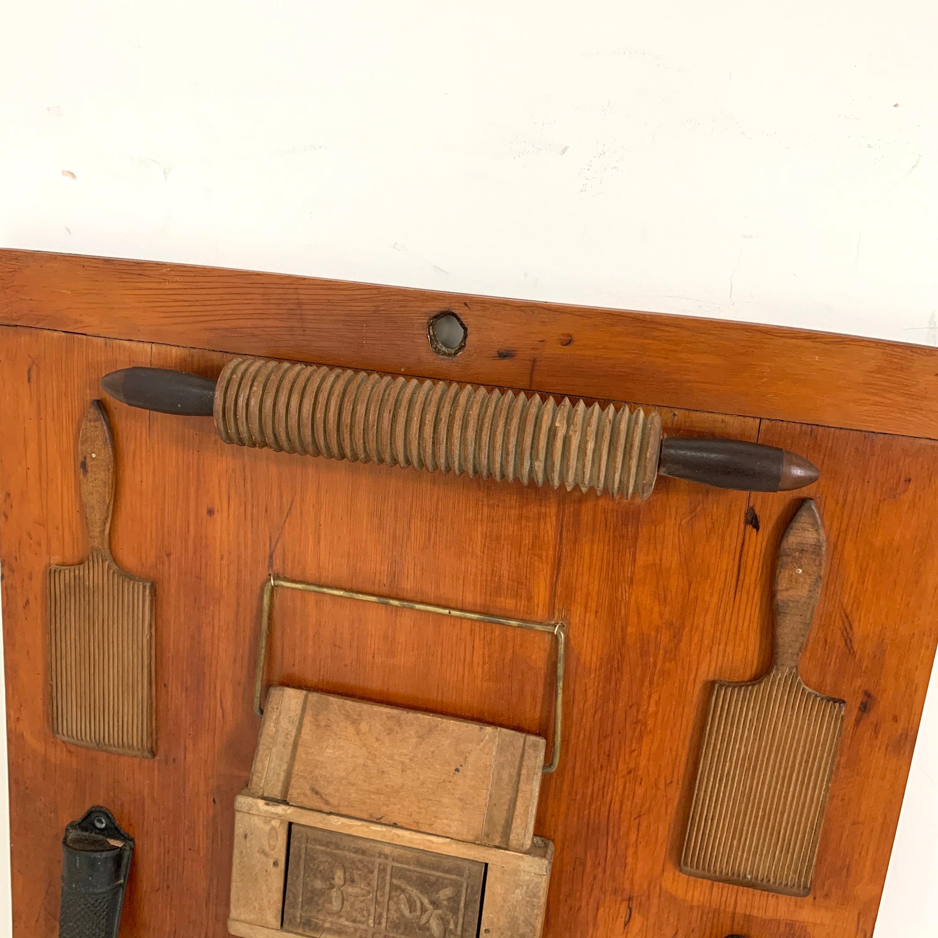 A charming sculptural modernist wall display of various 18th and 19th century tools relating to the art of baking, all mounted upon an antique breadboard. Signed on reverse “Virgil Sumner“ and dated 1949. At top are a pair of butter paddles, a three