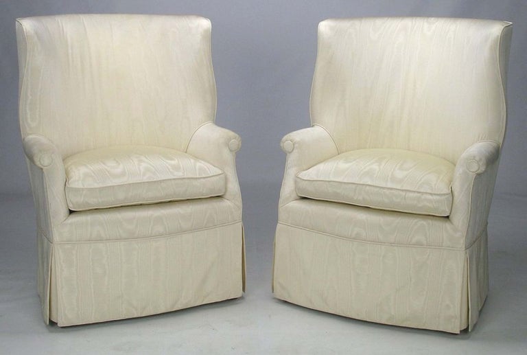 An elegant and unusual pair of wing chairs with curvaceous lines. The original upholstery is skirted, but the brass inlaid mahogany legs are quite nice in their own right. Wonderful ivory-white moire' fabric adds depth and texture.