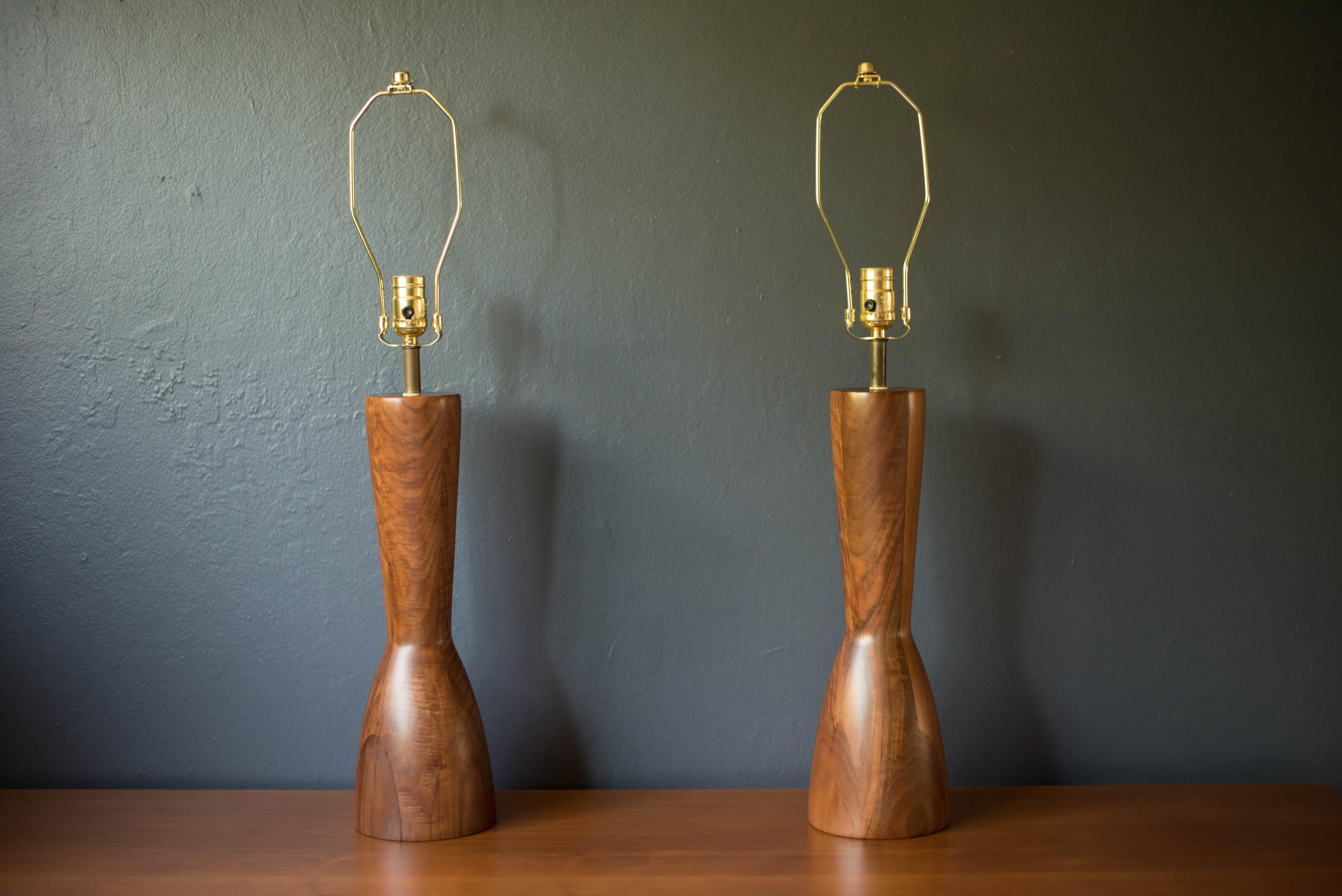 Vintage pair of solid staved walnut accent table lamps, circa 1960's. This lighting set features a unique sculptural shape accented with brass hardware and natural wood grains. Includes a three way switch mechanism. 

