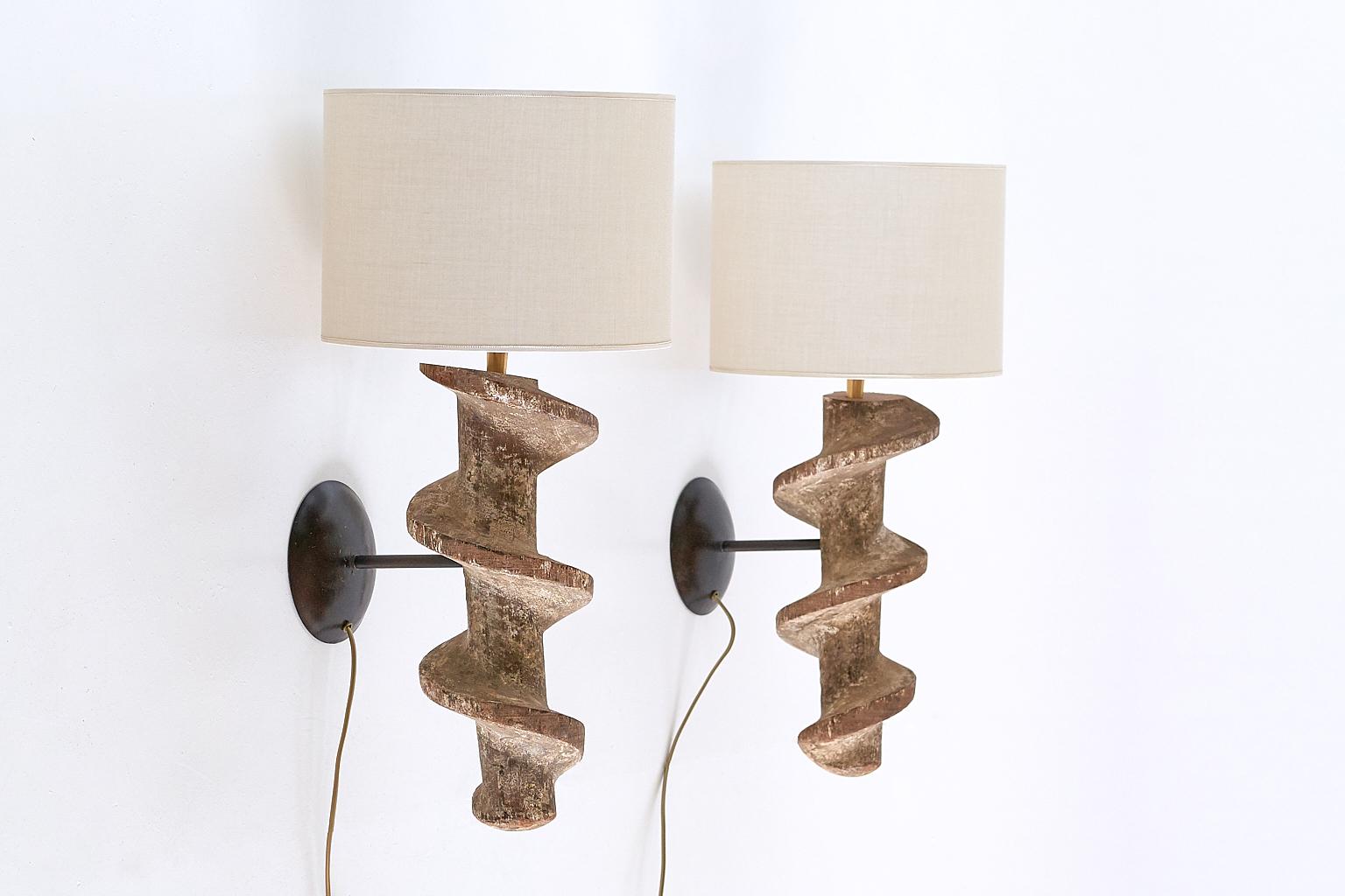 A unique and sculptural pair of wall lamps consisting of a striking spiral screw base in hardwood, wall bracket in black metal and custom fabric shades. 

The substantial concentric wooden spirals were used in the textile industry in the southern
