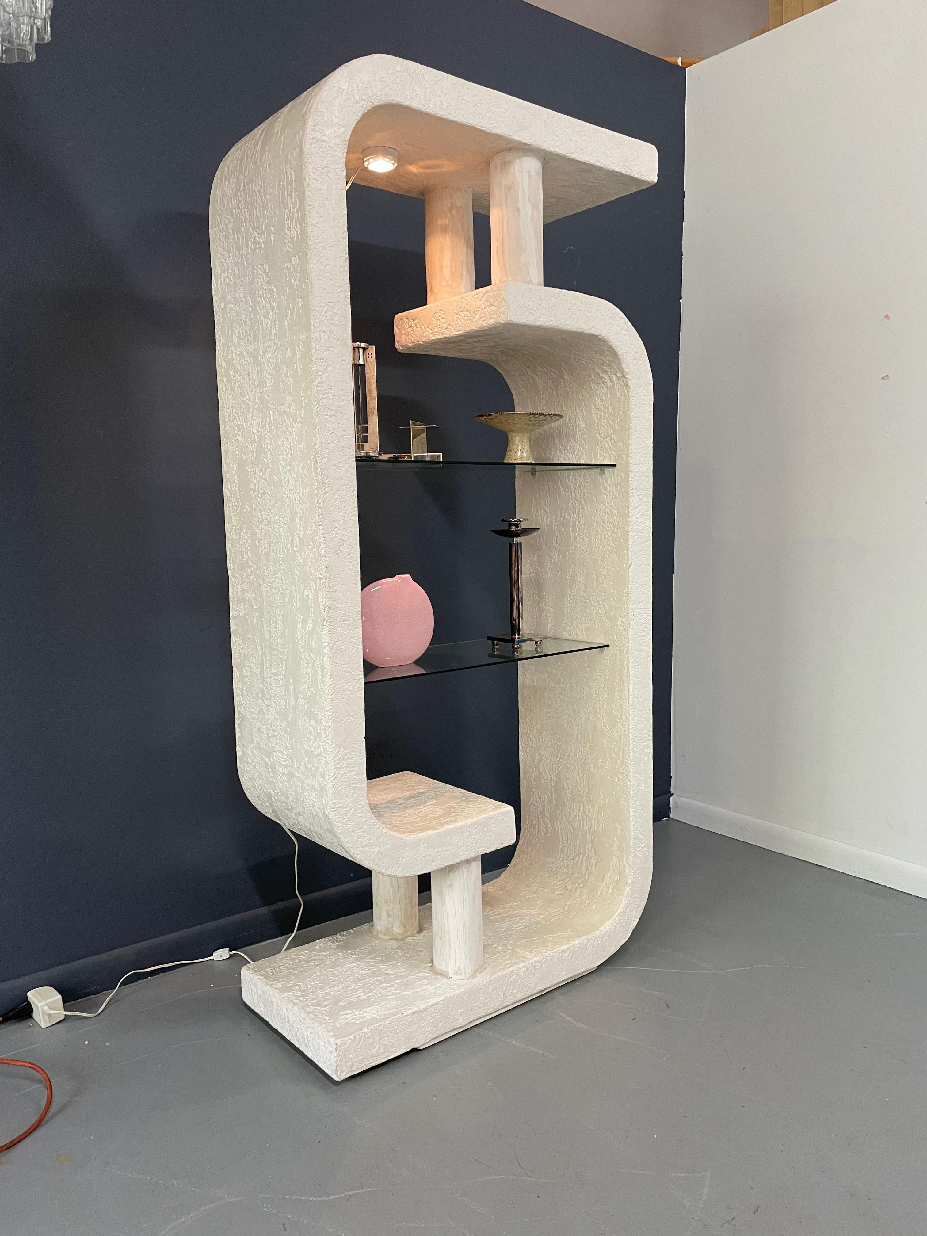 This sculptural shelf features a curved frame made of two C shaped pieces which are connected via two wood cylinders at the top and bottom. The two glass shelves can be illuminated from above.