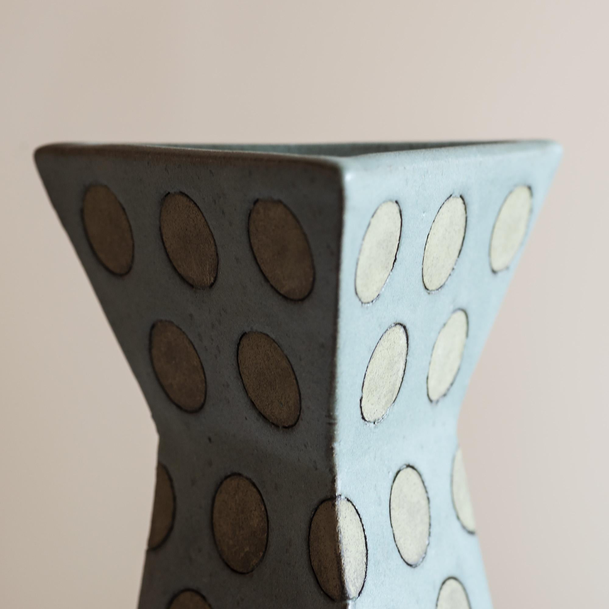 Triangular stoneware vase with polka dots in muted grey-green tones.
