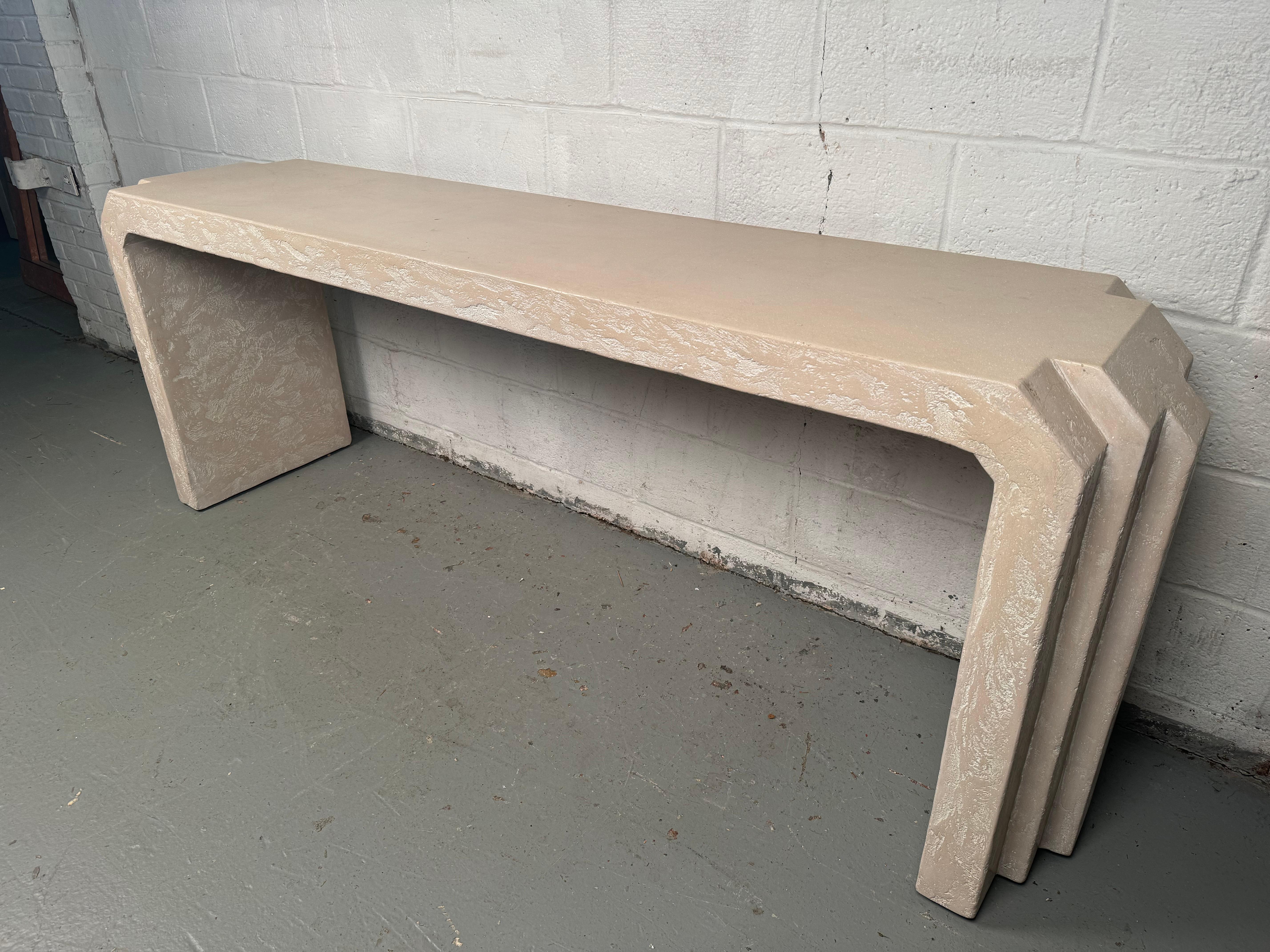 Eleva tu espacio con la atrevida sofisticación de esta consola escultórica postmoderna de escayola gris, una pieza que combina a la perfección arte y funcionalidad. Con su llamativa silueta minimalista y su acabado liso y texturizado, esta consola