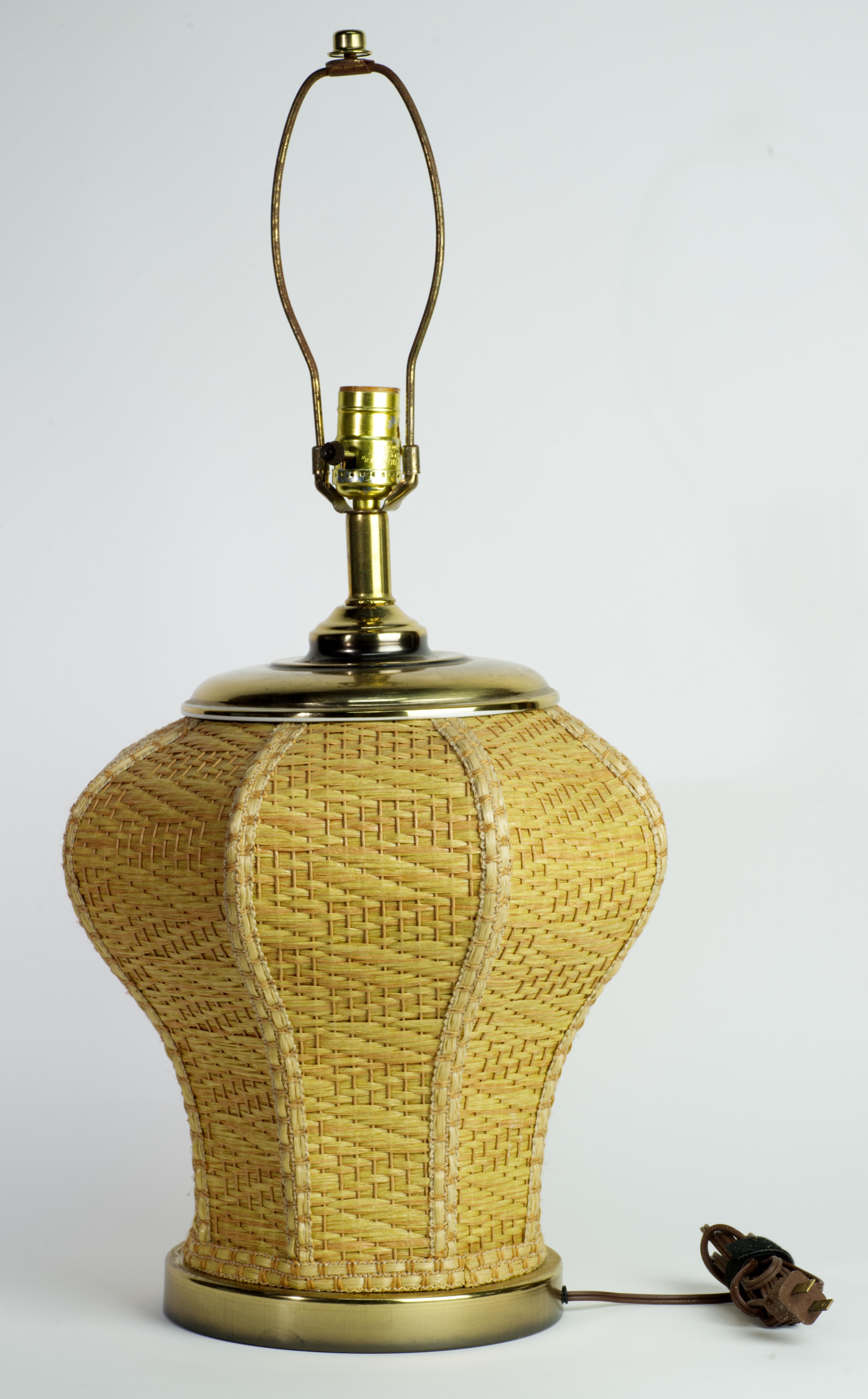  La rara lampada in rattan di vimini fatta a mano con base e piano in ottone ha una struttura architettonica curva, accentuata da un intreccio molto dettagliato. Il complesso intreccio sui lati della lampada è incorniciato da semplici nervature