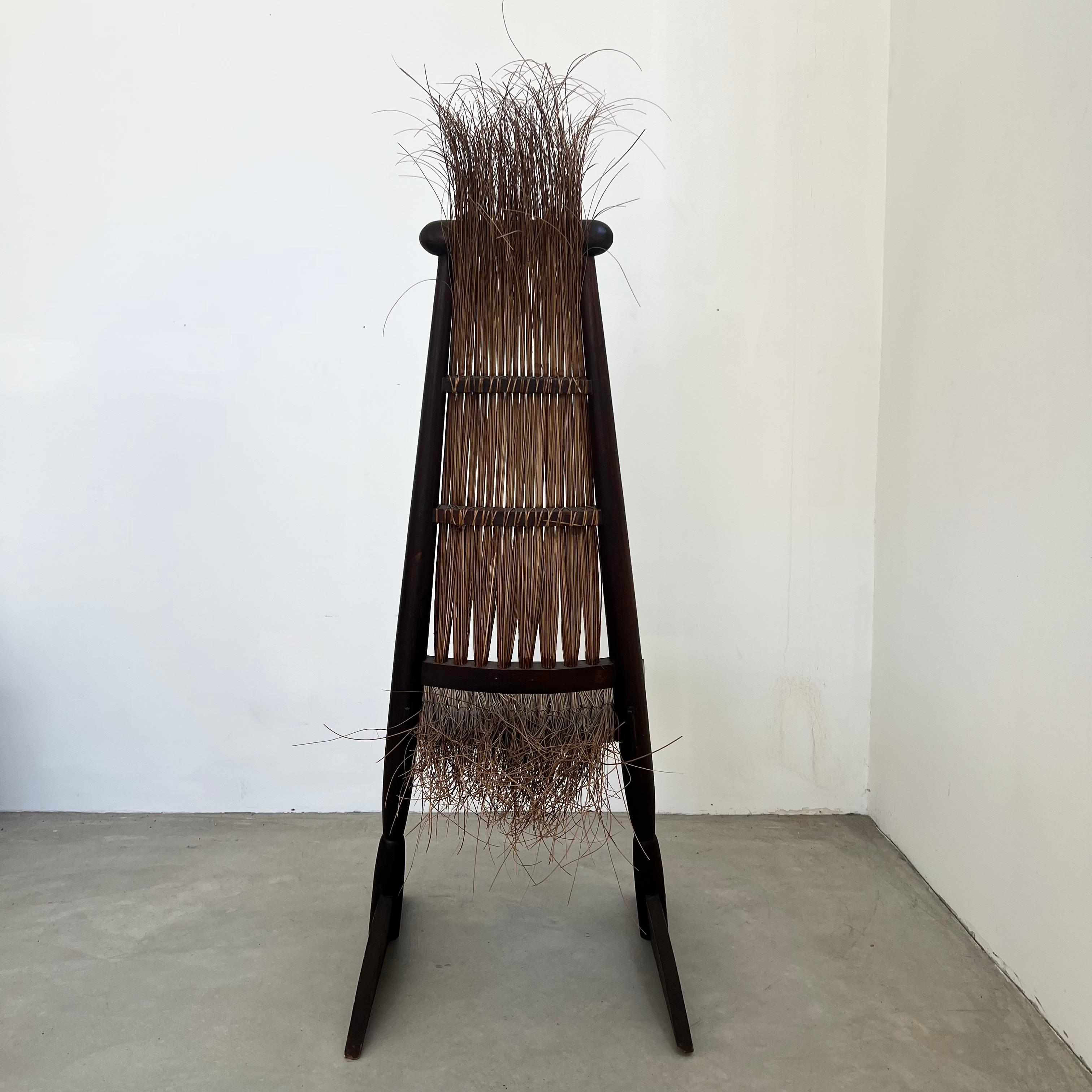Questa sedia all'avanguardia confonde il confine tra arte e arredamento. Lo schienale e la posizione angolare evocano un senso di movimento e tensione, mentre gli elementi in rattan intrecciato a mano apportano calore e consistenza organica, creando