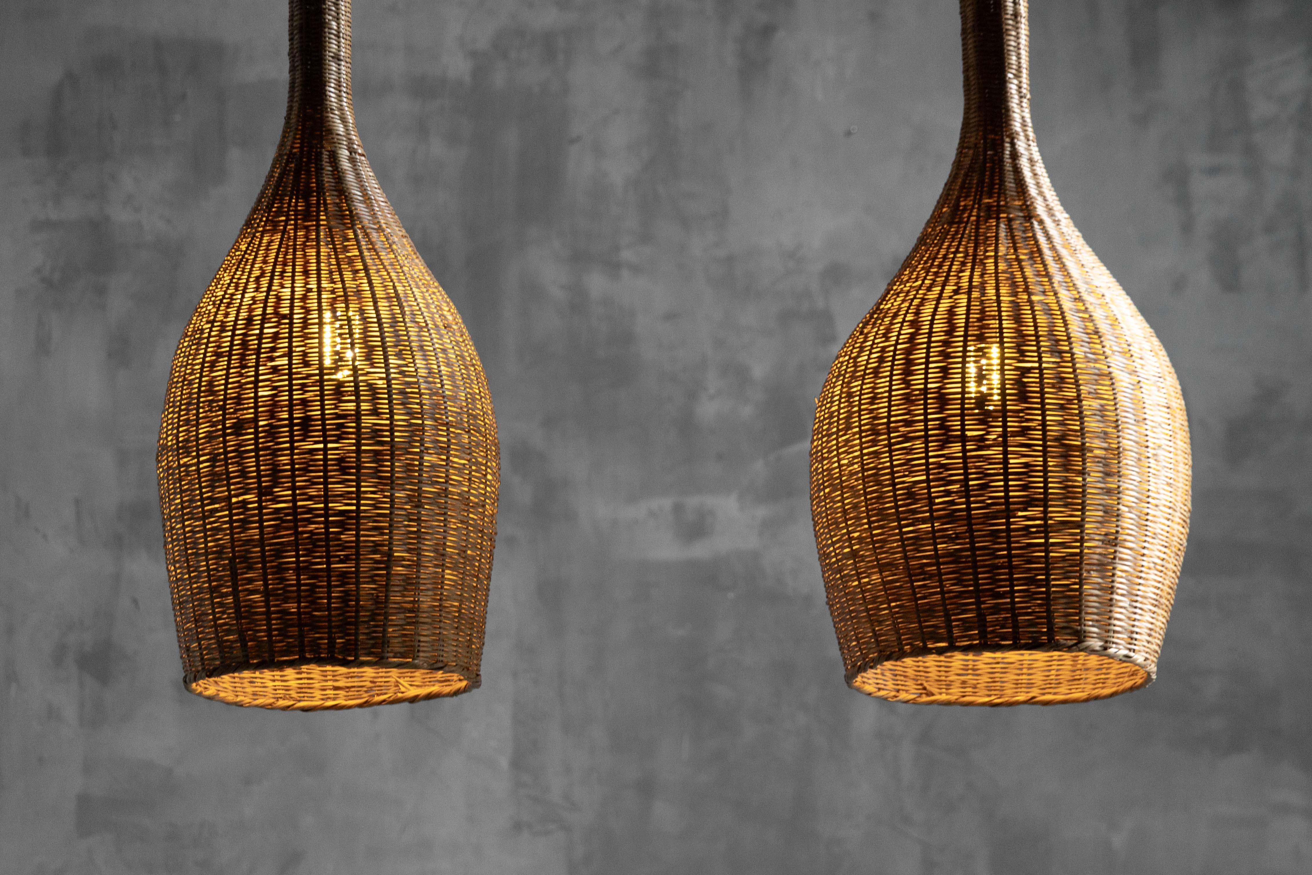 Zwei skulpturale Pendelleuchten aus Rattan aus der Mitte des Jahrhunderts, ca. 1960, mit langgestreckten Flaschensilhouetten, hohen schlanken Hälsen und abgerundeten Körpern, handgeflochten aus natürlichem Weidengeflecht, das beim Anzünden ein
