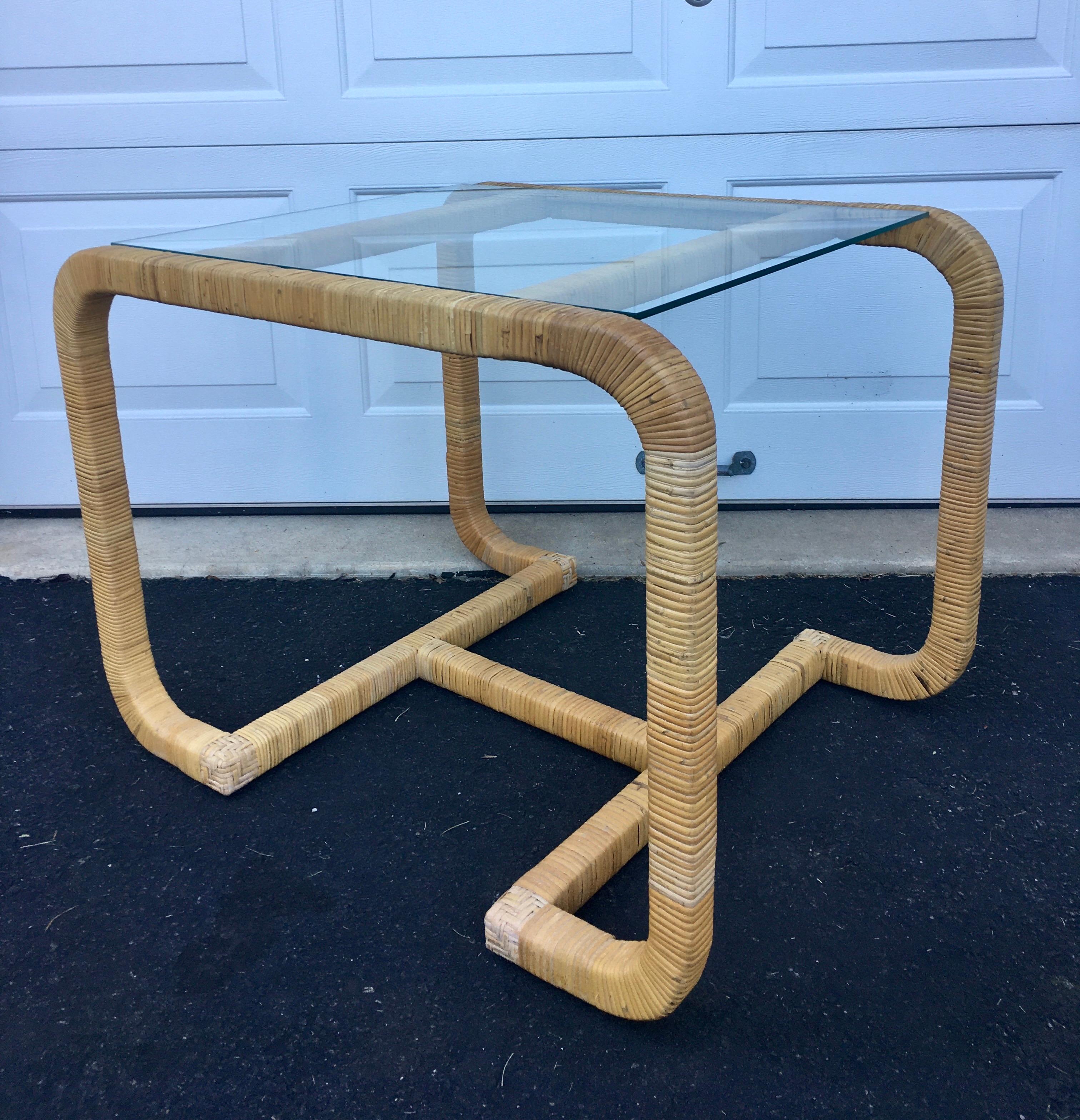 Vintage Mid-Century Modern rattan wrapped side or end table with clear glass top. Sculptural wood frame features an H-shaped base wrapped in natural toned rattan. Can be used as a bedside table or as a unique hall occasion center or cocktail table.
