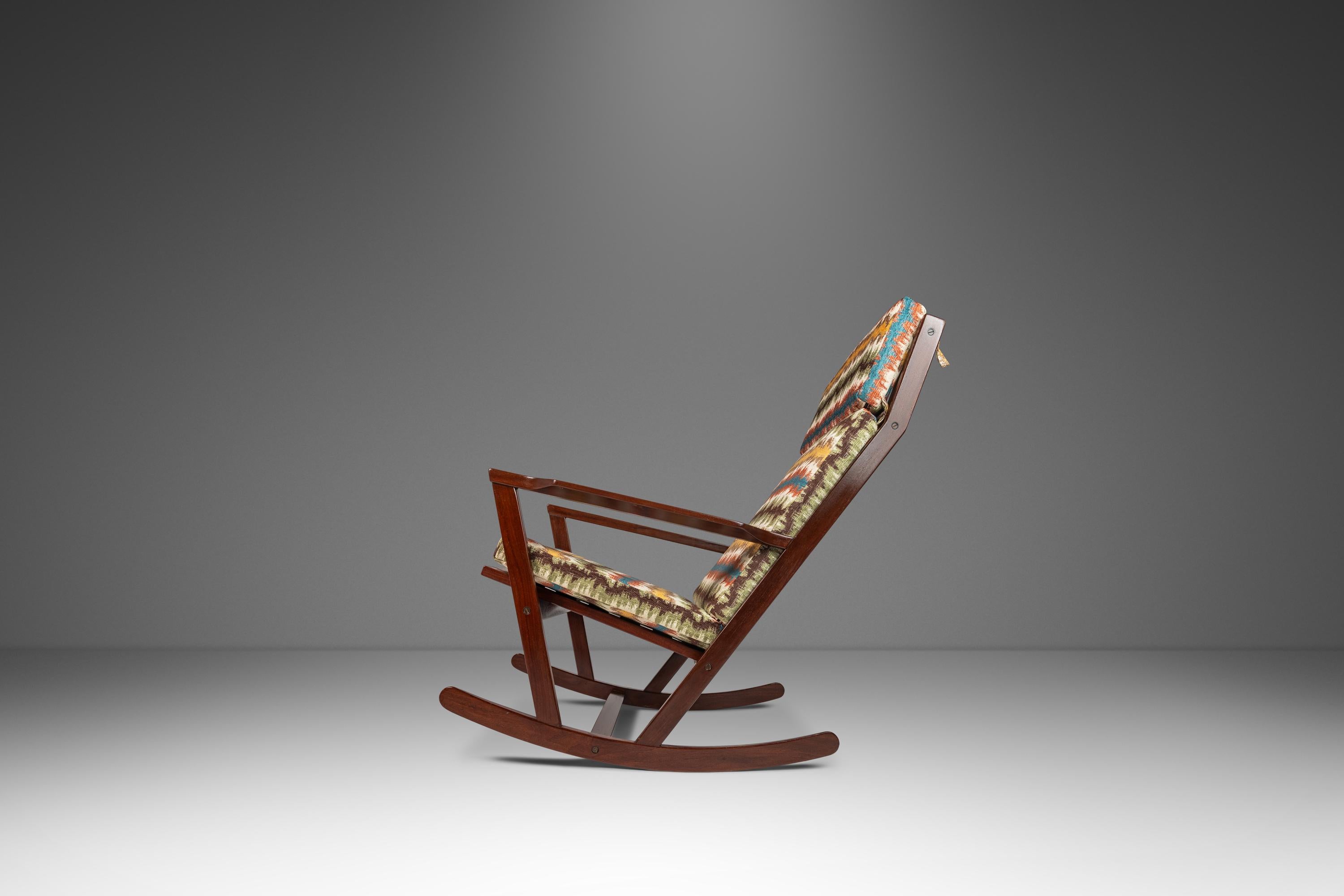 Ti presentiamo una rara sedia a dondolo di produzione danese disegnata dall'influente Poul Volther per Frem Rojle Frem. Costruita con un'elegante struttura in mogano massiccio con ricche venature del legno e rivestita in un favoloso tessuto di