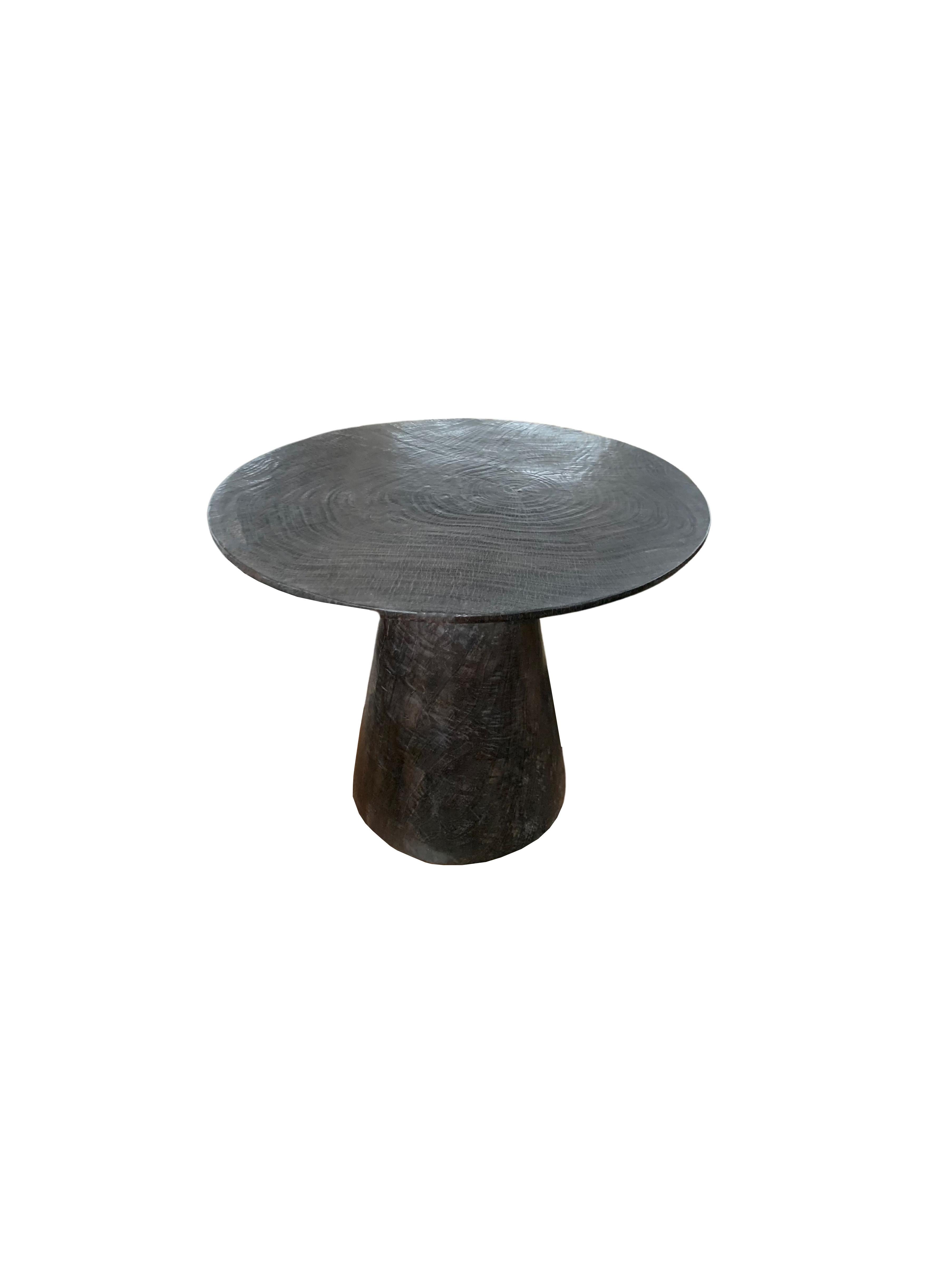 Une table d'appoint ronde merveilleusement sculpturale avec une finition brûlée. Pour obtenir son pigment sombre, le bois a été brûlé à de nombreuses reprises, poncé et recouvert d'une couche transparente. Son pigment neutre et sa texture boisée