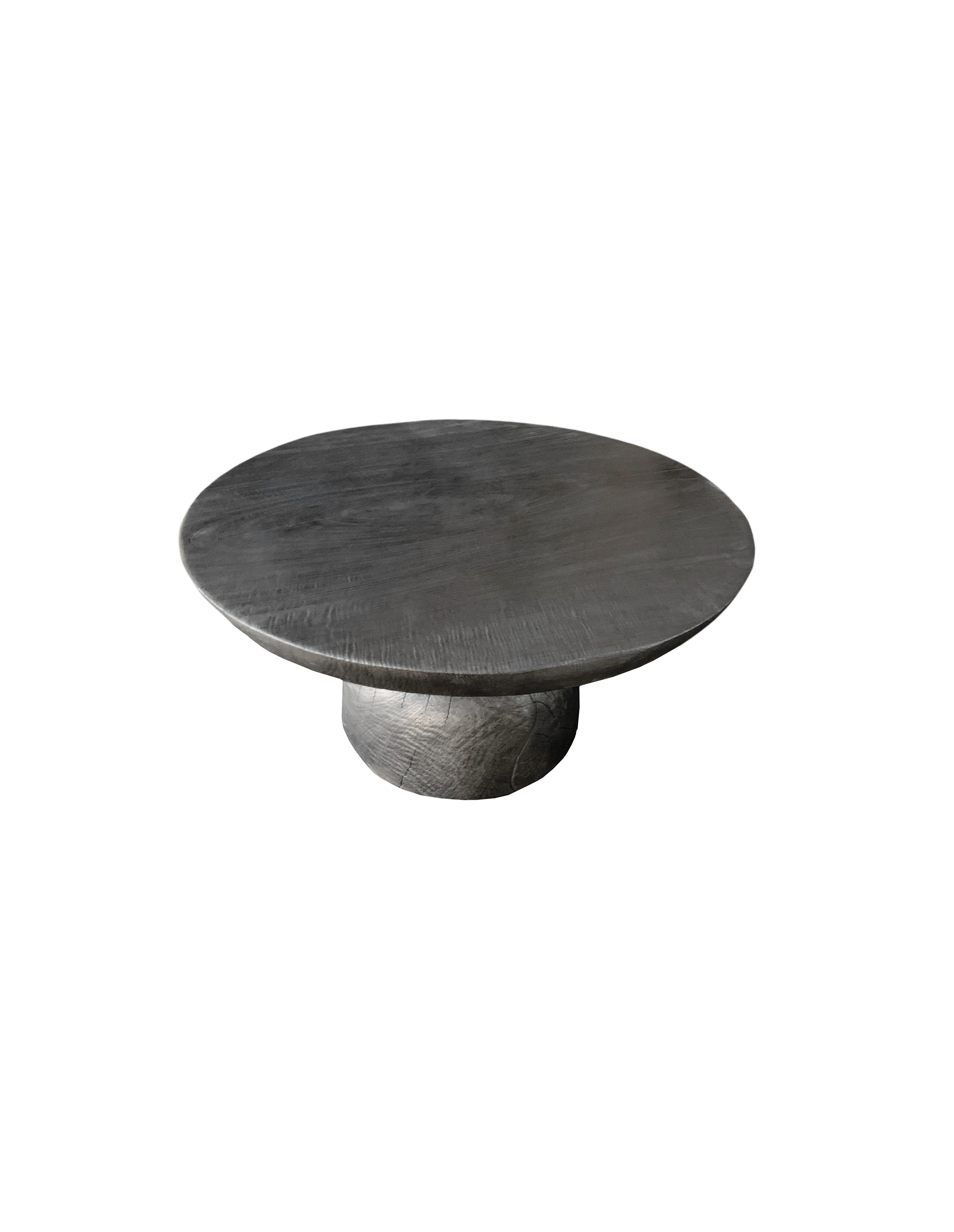 Une table d'appoint ronde merveilleusement sculpturale avec une finition brûlée. Son pigment neutre et sa texture bois en font un produit parfait pour tout espace. Elle présente une base effilée et un grand plateau rond. Une pièce unique,