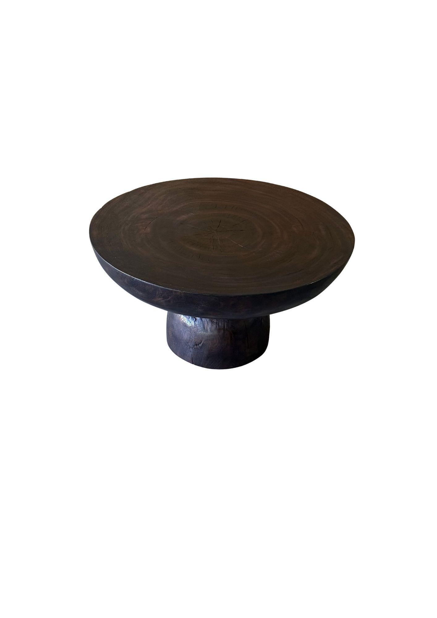 Una mesa auxiliar redonda maravillosamente escultural con un acabado espresso, quemado varias veces, lijado y alisado a la perfección con un acabado de capa transparente. Su pigmento neutro y su textura de madera lo hacen perfecto para cualquier