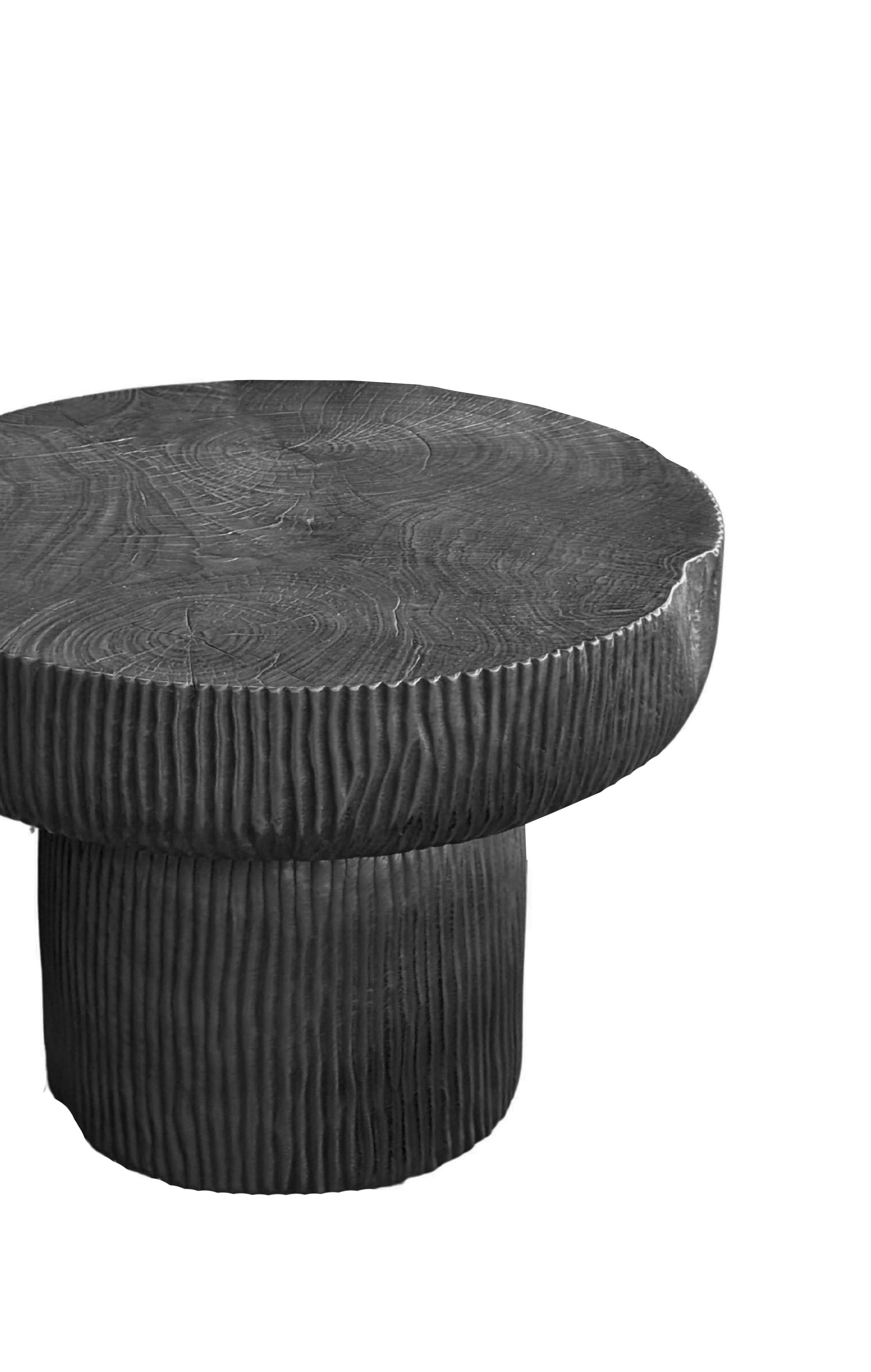 A study in form, texture, and craftsmanship, this round side table is expertly handcrafted from solid mango wood and finished in a deep burnt black that accentuates the wood’s natural grain. Its smooth, circular top rests on a seamless cylindrical