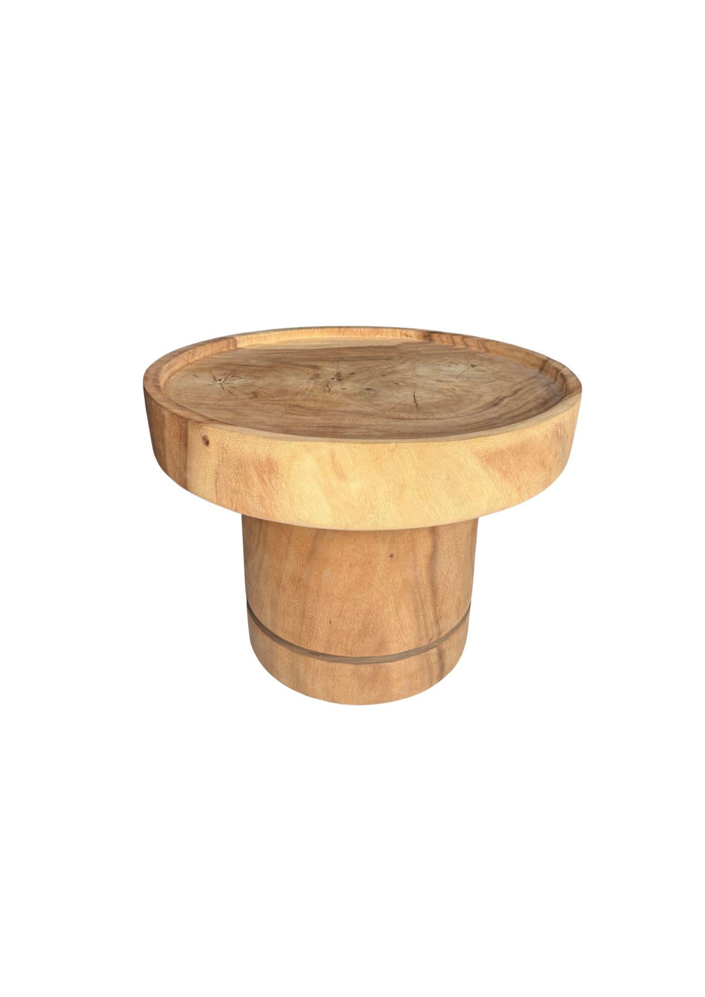 Crafted from solid mango wood, this sculptural sofa table combines bold form with natural elegance. Its smooth, rounded silhouette highlights the organic grain patterns of the wood. The wide tabletop rests on a sturdy, cylindrical base carved from