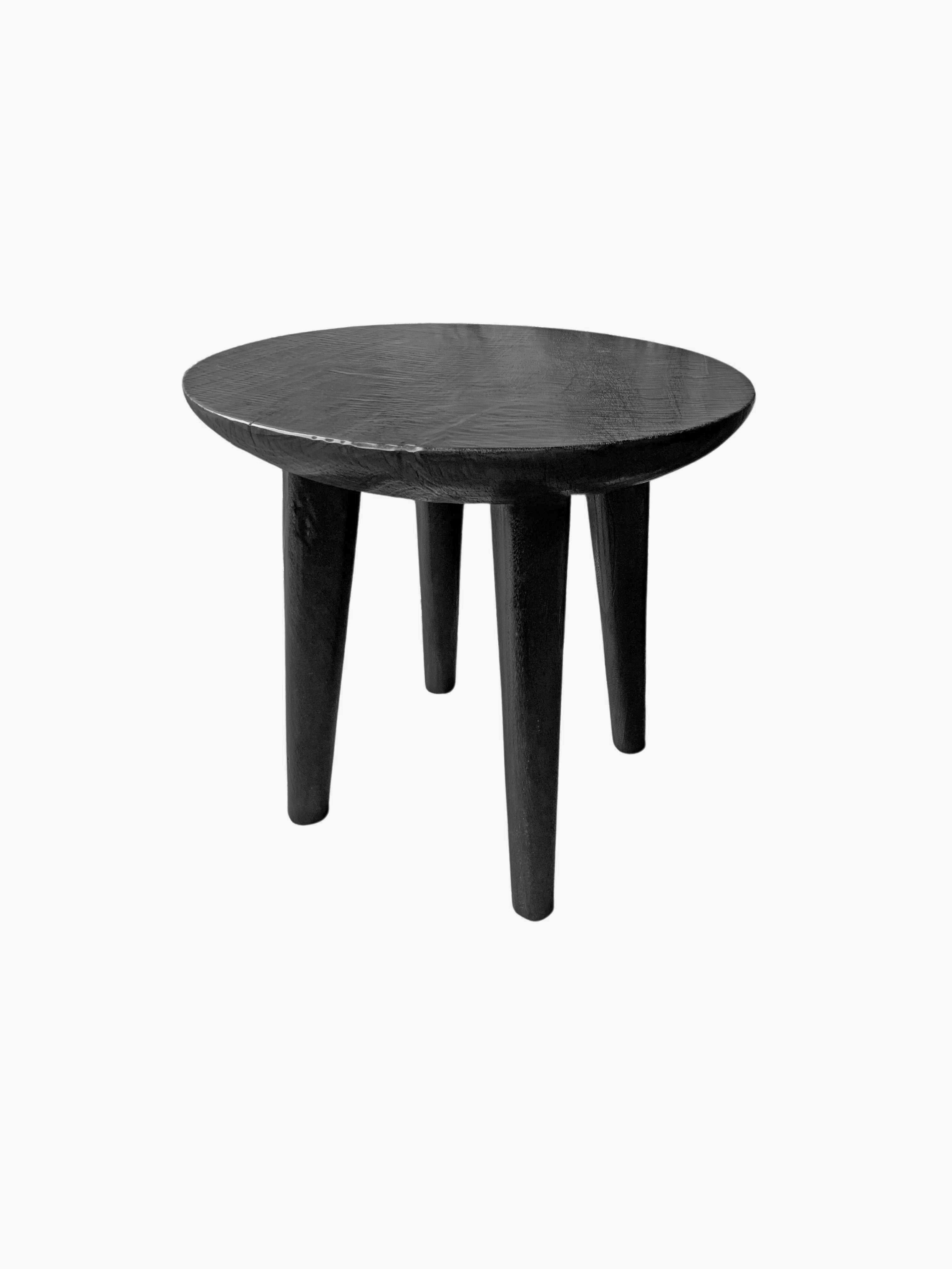 A wonderfully sculptural round side table with narrowly proportioned legs. Its stark black pigment was achieved through burning the wood three times. Its neutral pigment and subtle wood texture makes it perfect for any space. A uniquely sculptural
