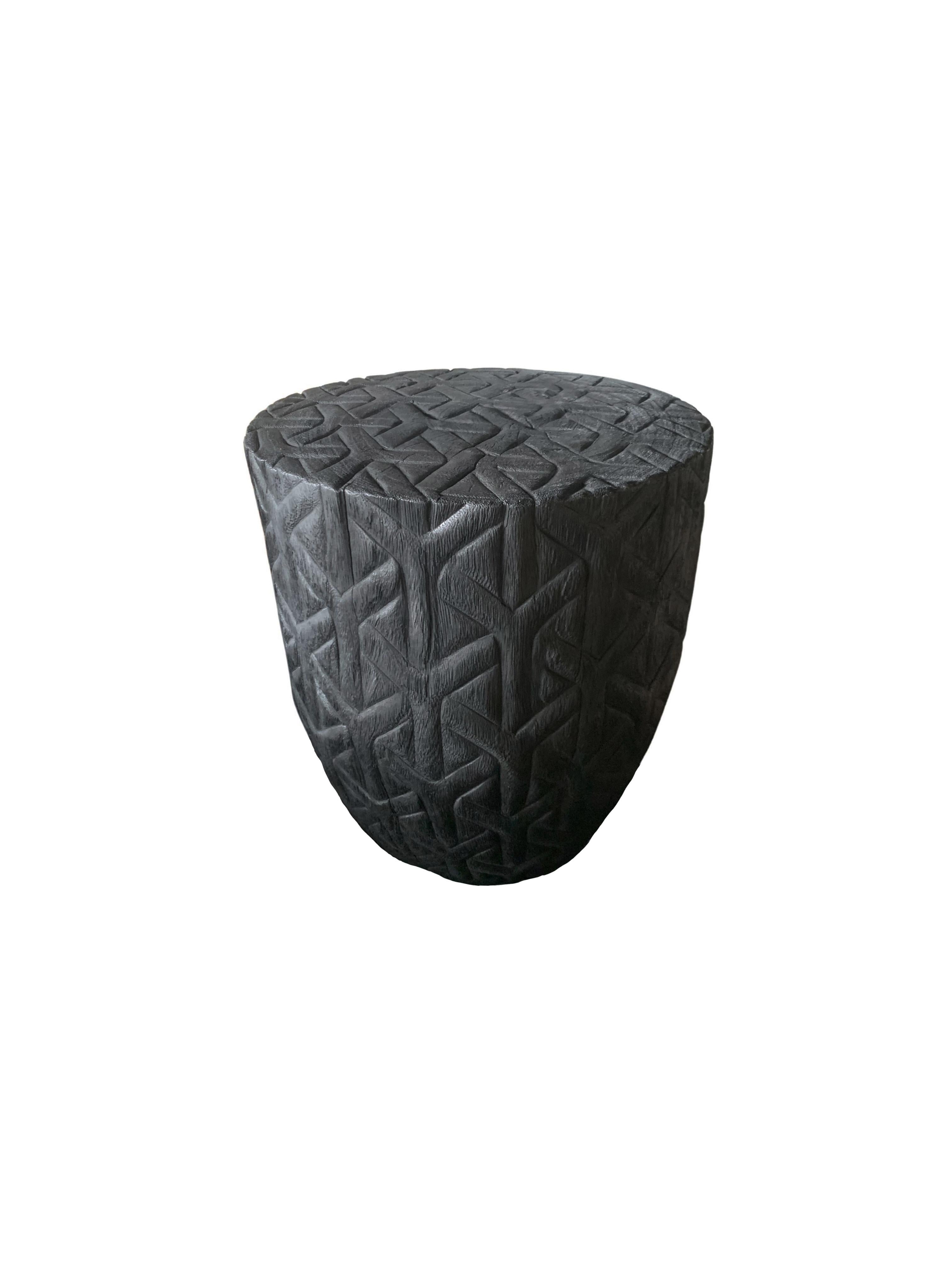 A wonderfully sculptural side table with a geometric pattern hand-carved on all sides. Its rich black pigment was achieved through burning the wood three times. Its neutral pigment and subtle wood texture makes it perfect for any space. A uniquely