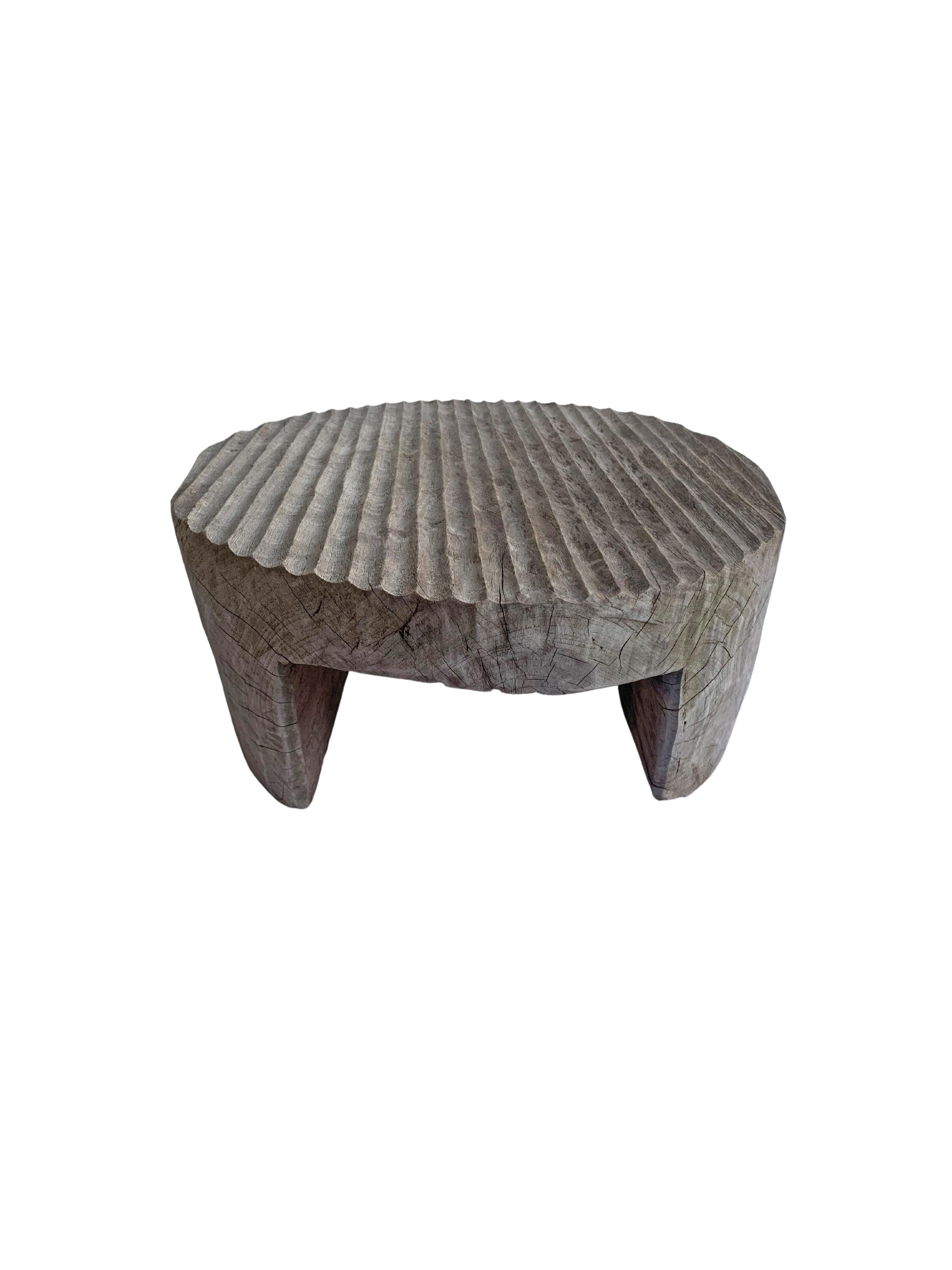 This side table was crafted from a single block of teak wood. A wonderfully sculptural round side table. Its neutral pigment and subtle wood texture makes it perfect for any space. It features a carved ribbed design on its topside which adds to its