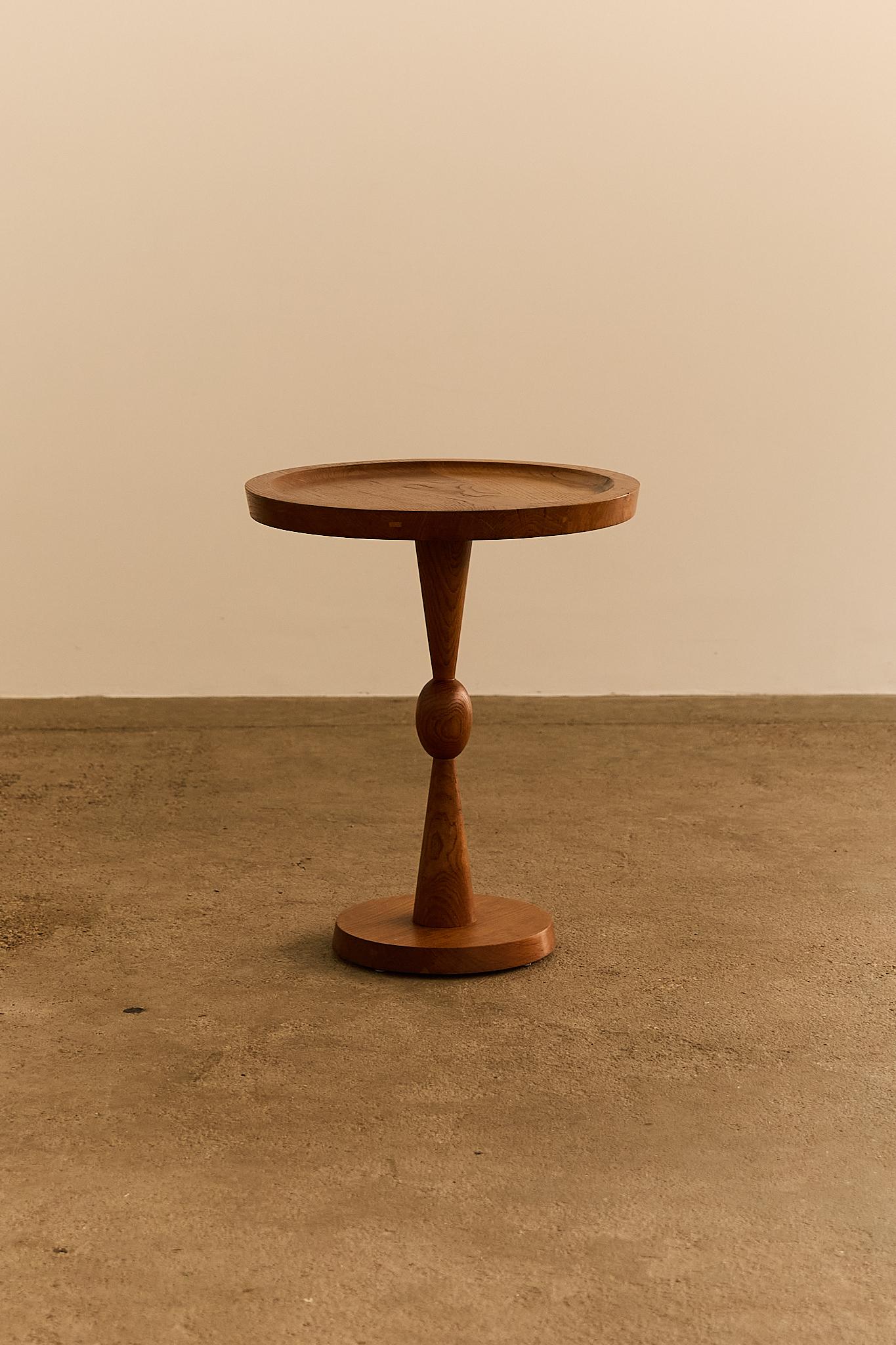 A beautifully crafted side table from the 1960s, made of solid wood with a warm, natural finish. The round tabletop features a subtle raised lip; Its sculptural base showcases refined turning work, balancing a tapering cone and rounded central
