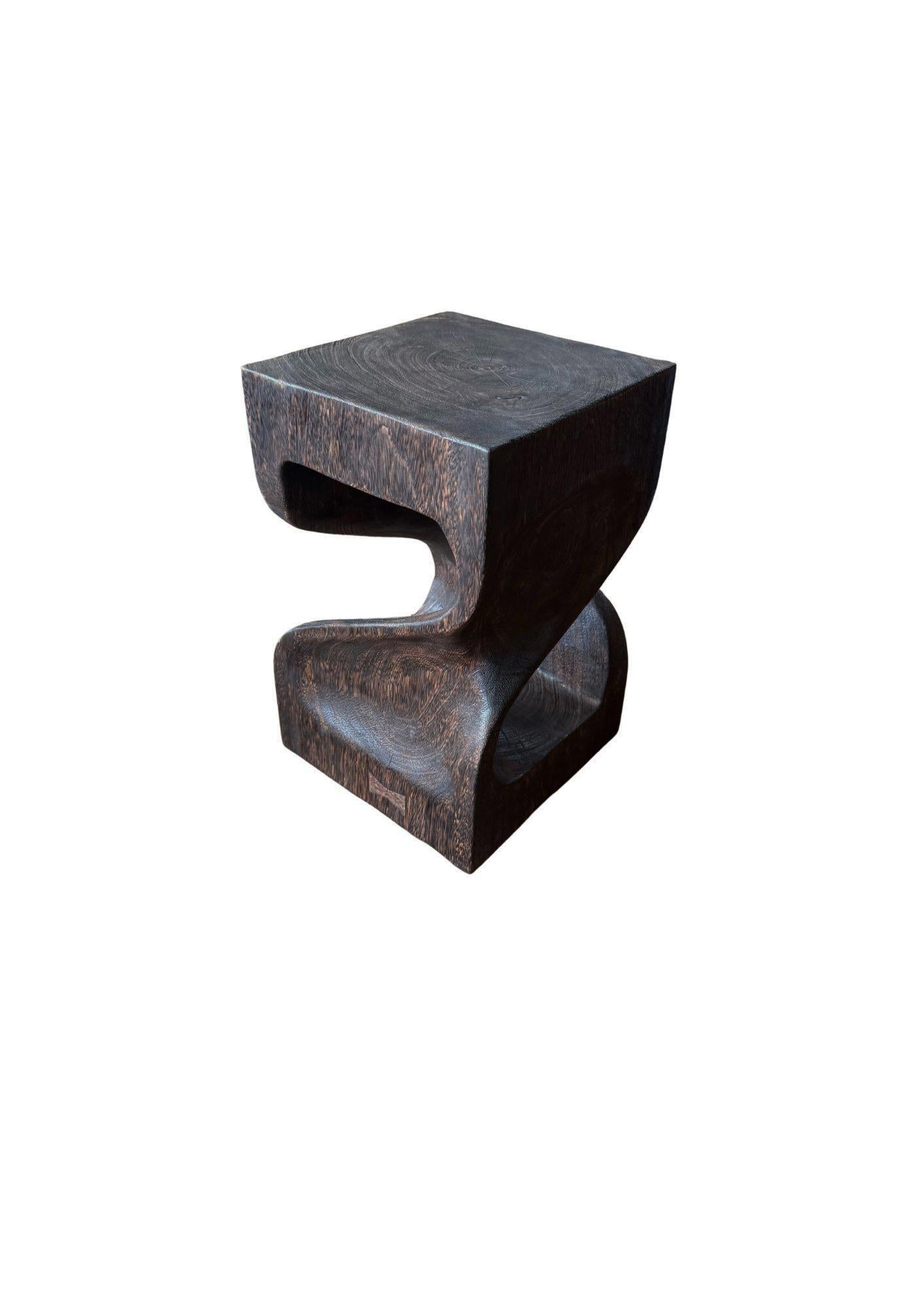 Sculptée à la main dans du bois de suar massif, cette table d'appoint remarquable présente une forme fluide et sculpturale qui allie des courbes organiques à des lignes audacieuses et modernes. Chaque pièce est méticuleusement brûlée plusieurs fois