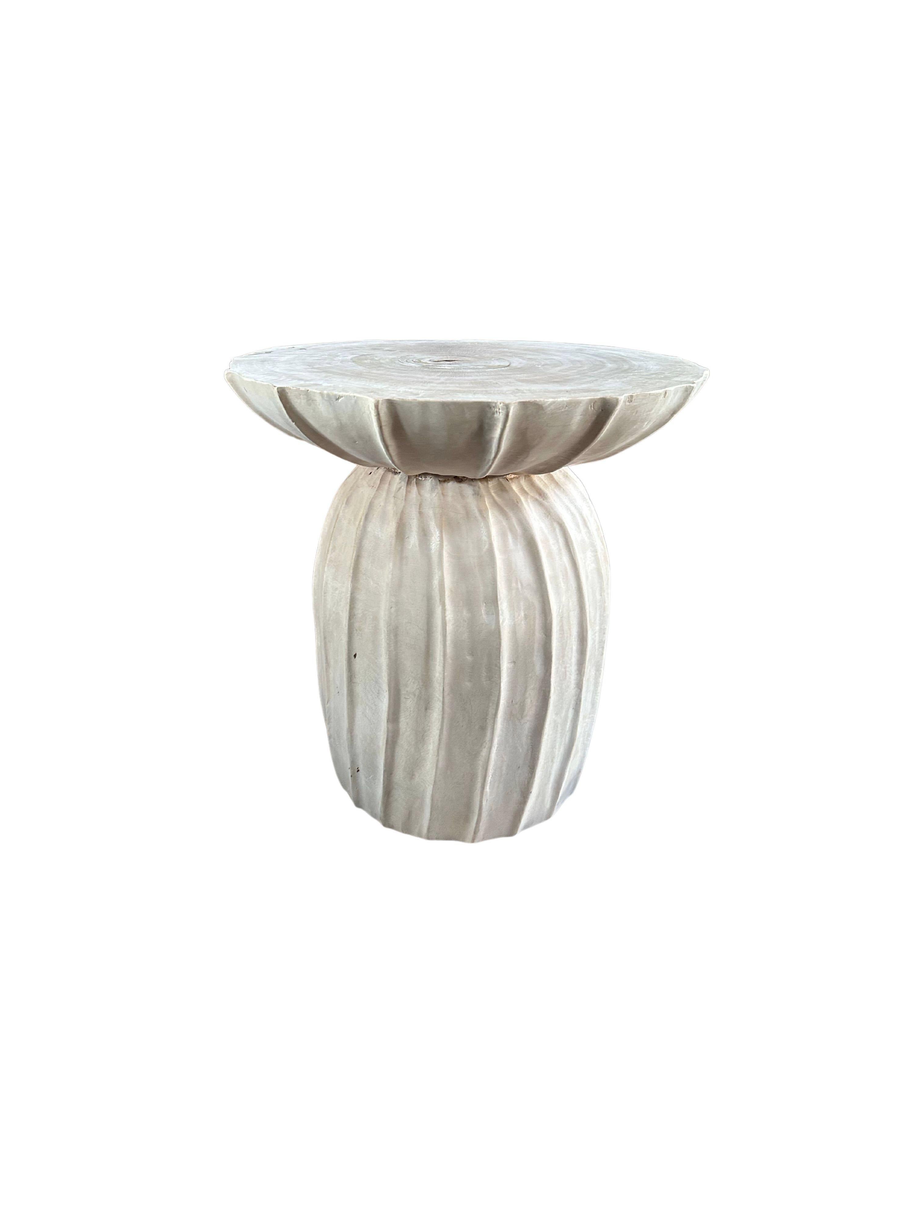 This wonderfully sculptural round side table features a ribbed pattern along its sides. The table's neutral pigment makes it perfect for any space. It was crafted from a solid block of mango wood and has elegant contours resembling a flowing form.