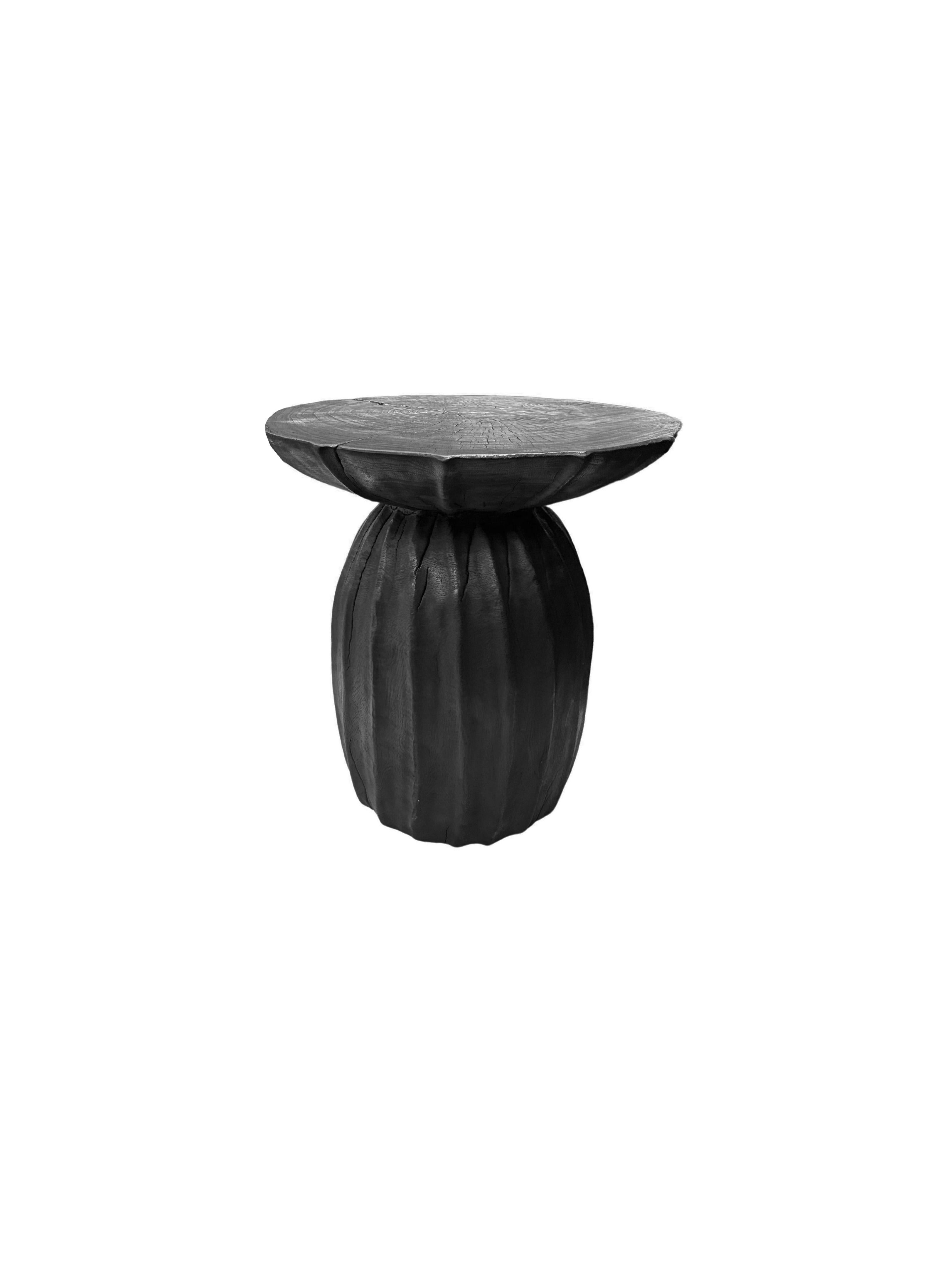 Cette table d'appoint ronde merveilleusement sculpturale présente un motif nervuré sur ses côtés. Le pigment neutre de la table lui permet de s'intégrer parfaitement dans n'importe quel espace. Il a été fabriqué à partir d'un bloc massif de bois de