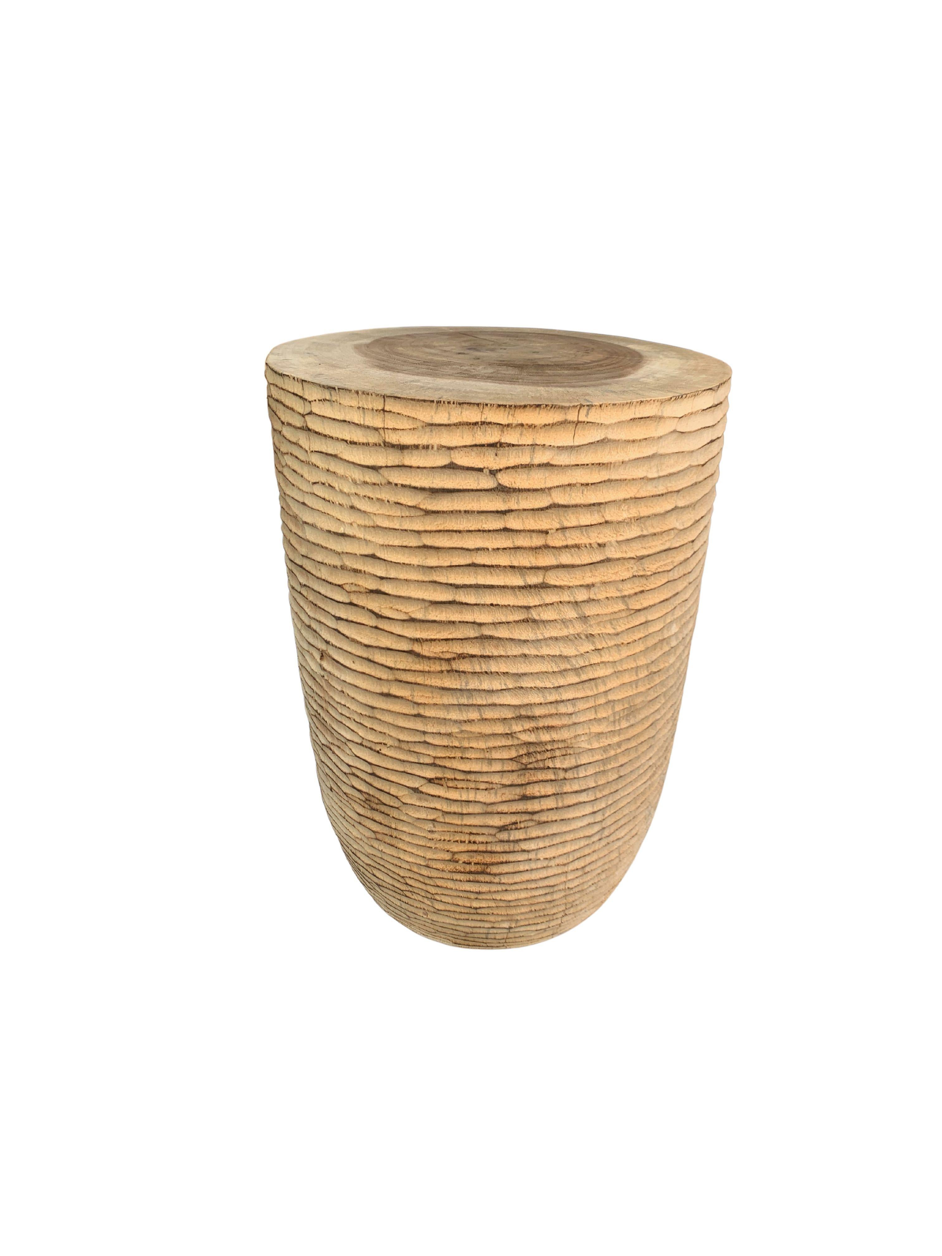 In its raw organic form, this wonderfully sculptural round side table features an elaborate hand hewn texture on its sides. Its narrow slender shape and mix of curves adds to its charm. The table's neutral pigment makes it perfect for any space. A