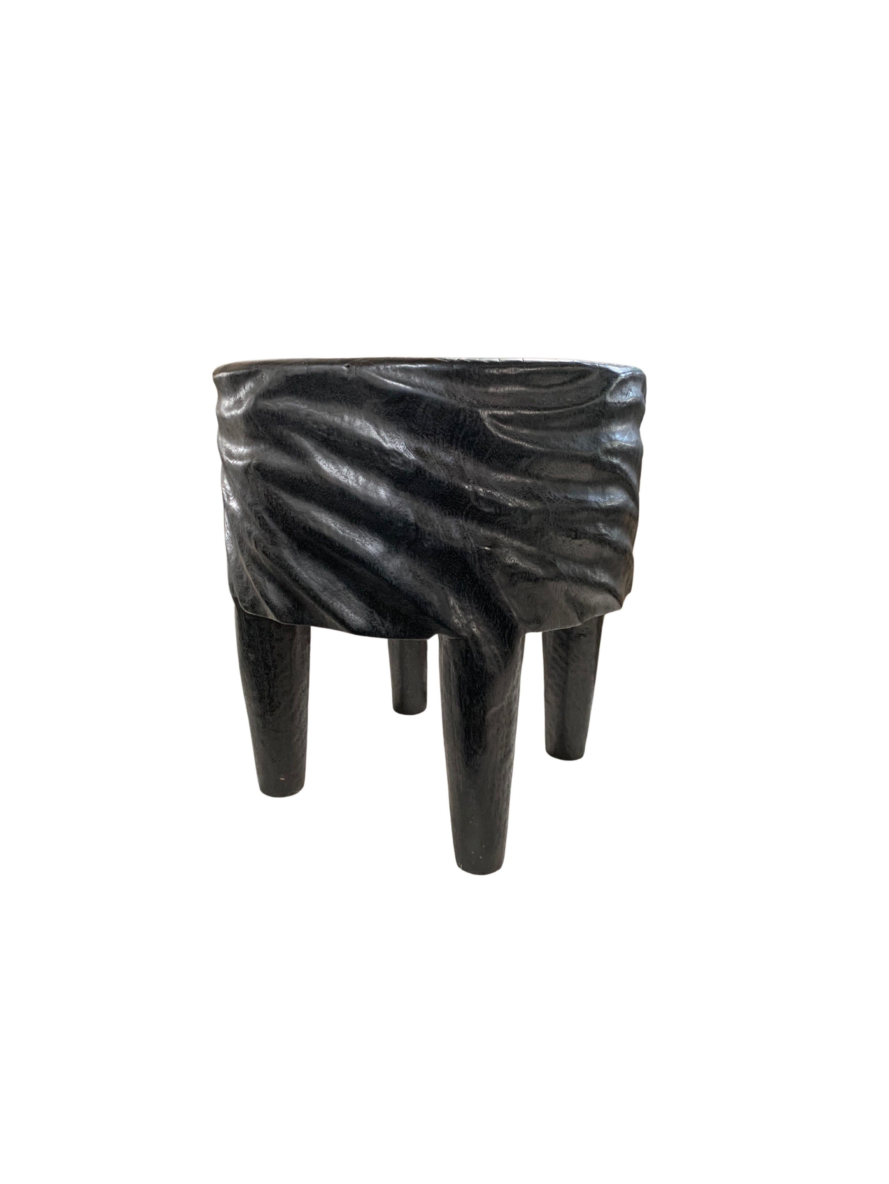 A wonderfully sculptural round side table with a hand-carved design around its exterior and four elongated legs. Its rich black pigment was achieved through burning the wood three times. Its neutral pigment and subtle wood texture makes it perfect