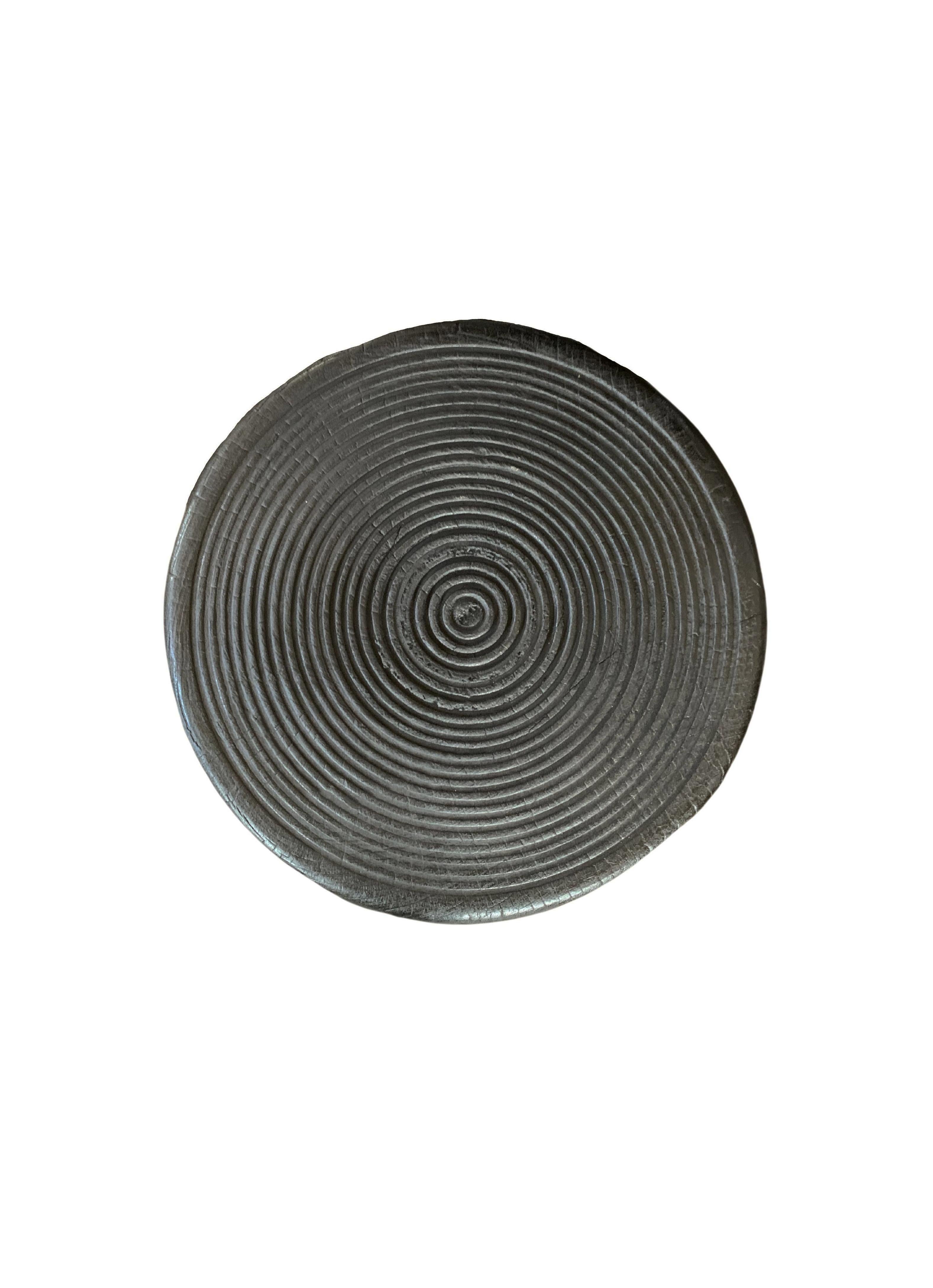 Una mesa auxiliar redonda maravillosamente escultural con un diseño acanalado tallado a mano en su parte superior. Su rico pigmento negro se consiguió quemando la madera tres veces. Su pigmento neutro y su sutil textura de madera lo hacen perfecto