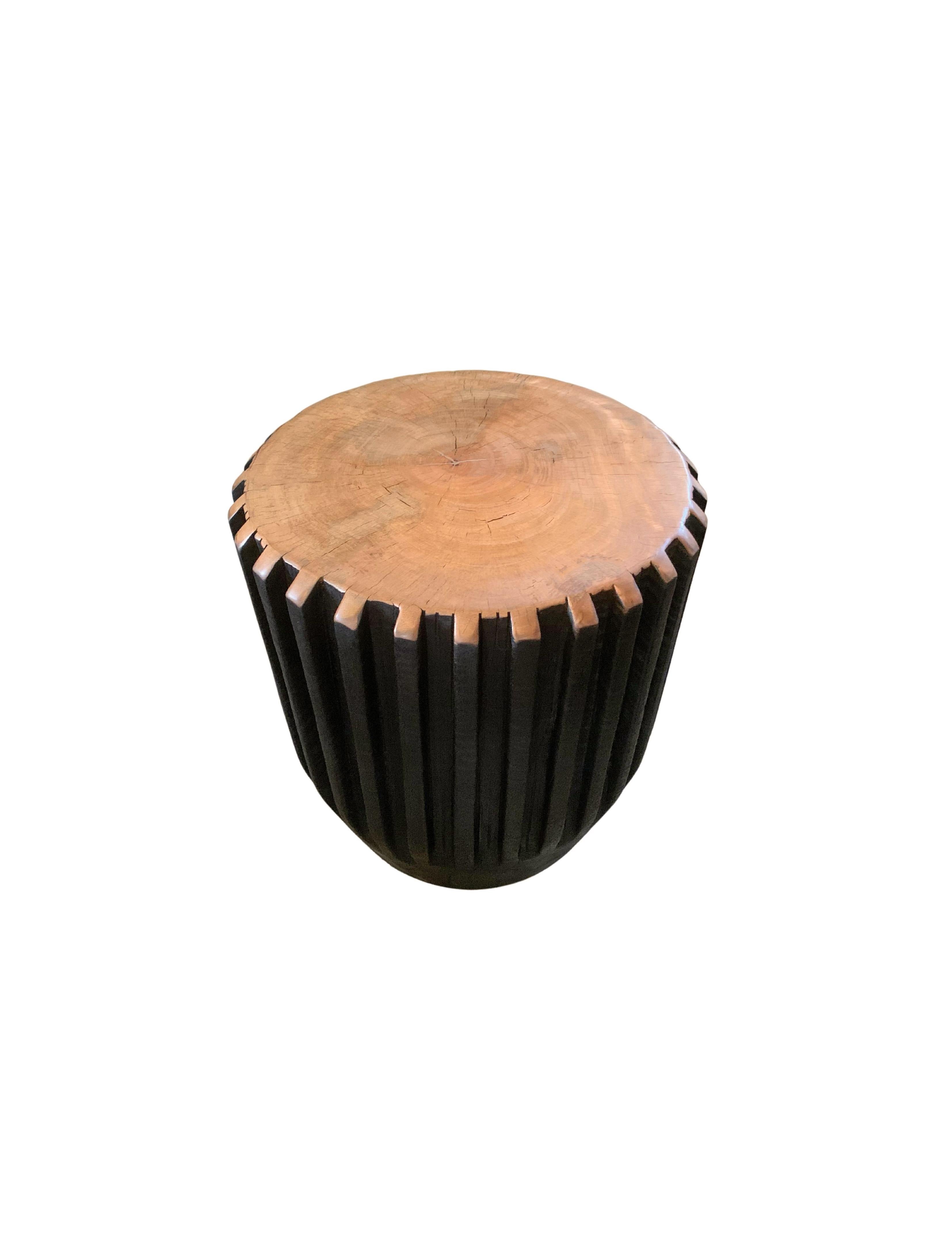 A wonderfully sculptural round side table with a hand-carved, ribbed design on its exterior. Its rich black pigment was achieved through burning the wood three times. Its top side does not possess a burnt finish but a natural polished finished
