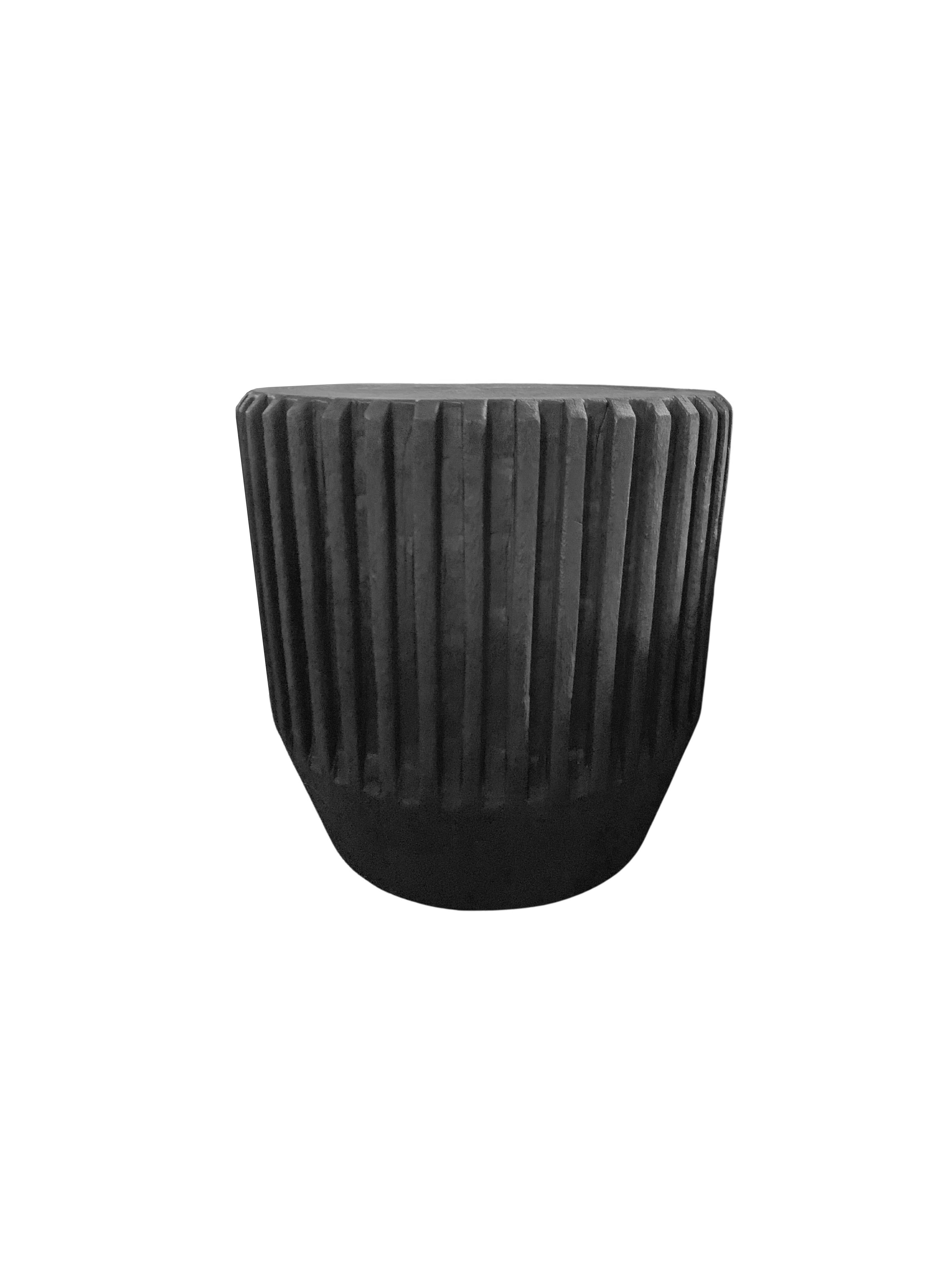 A wonderfully sculptural round side table with a hand-carved, ribbed design on its exterior. Its rich black pigment was achieved through burning the wood three times. Its neutral pigment and subtle wood texture makes it perfect for any space. A