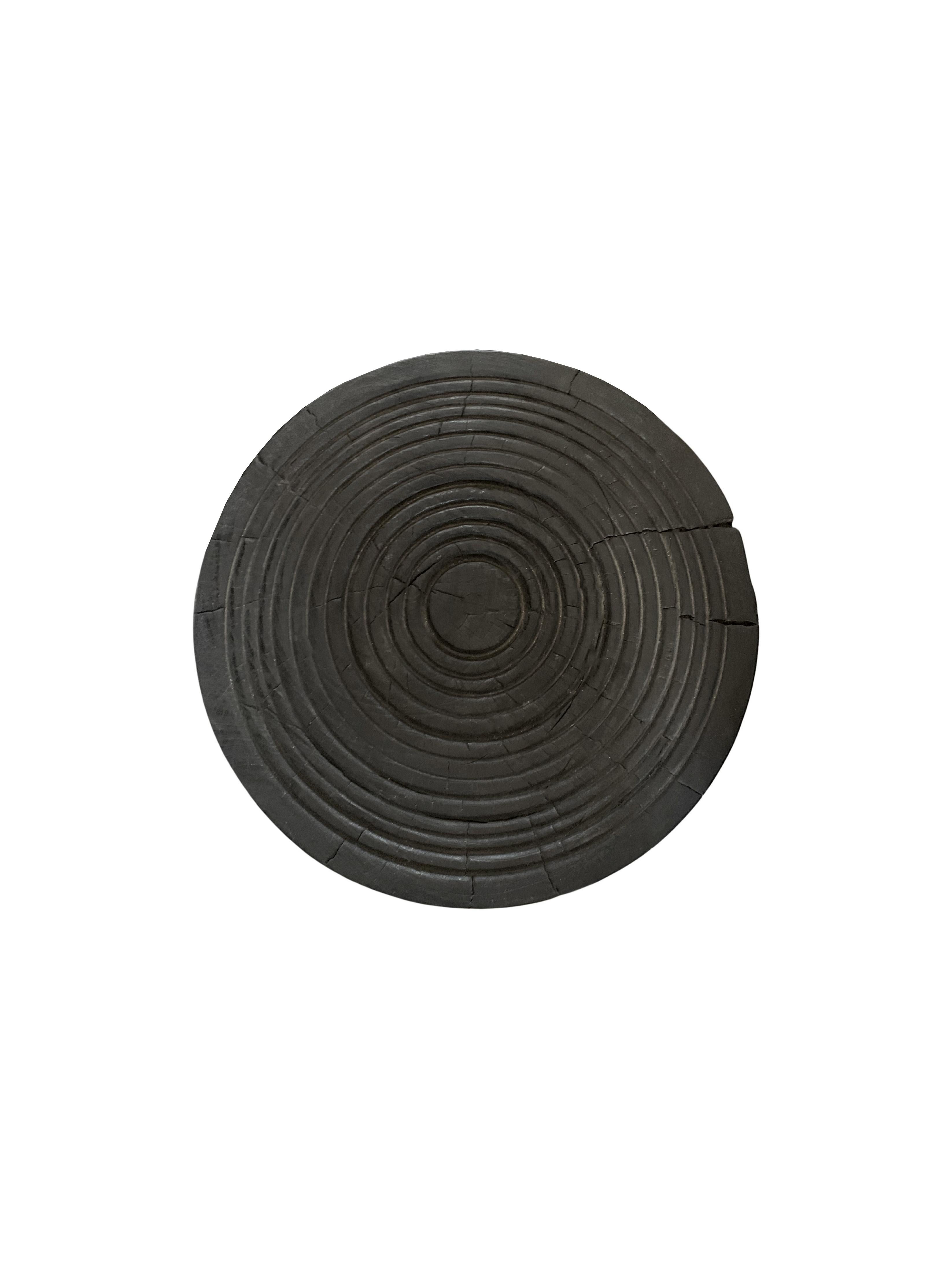 A wonderfully sculptural round side table with a hand-carved, ribbed design on its top side. Its rich black pigment was achieved through burning the wood three times. Its neutral pigment and subtle wood texture makes it perfect for any space. A
