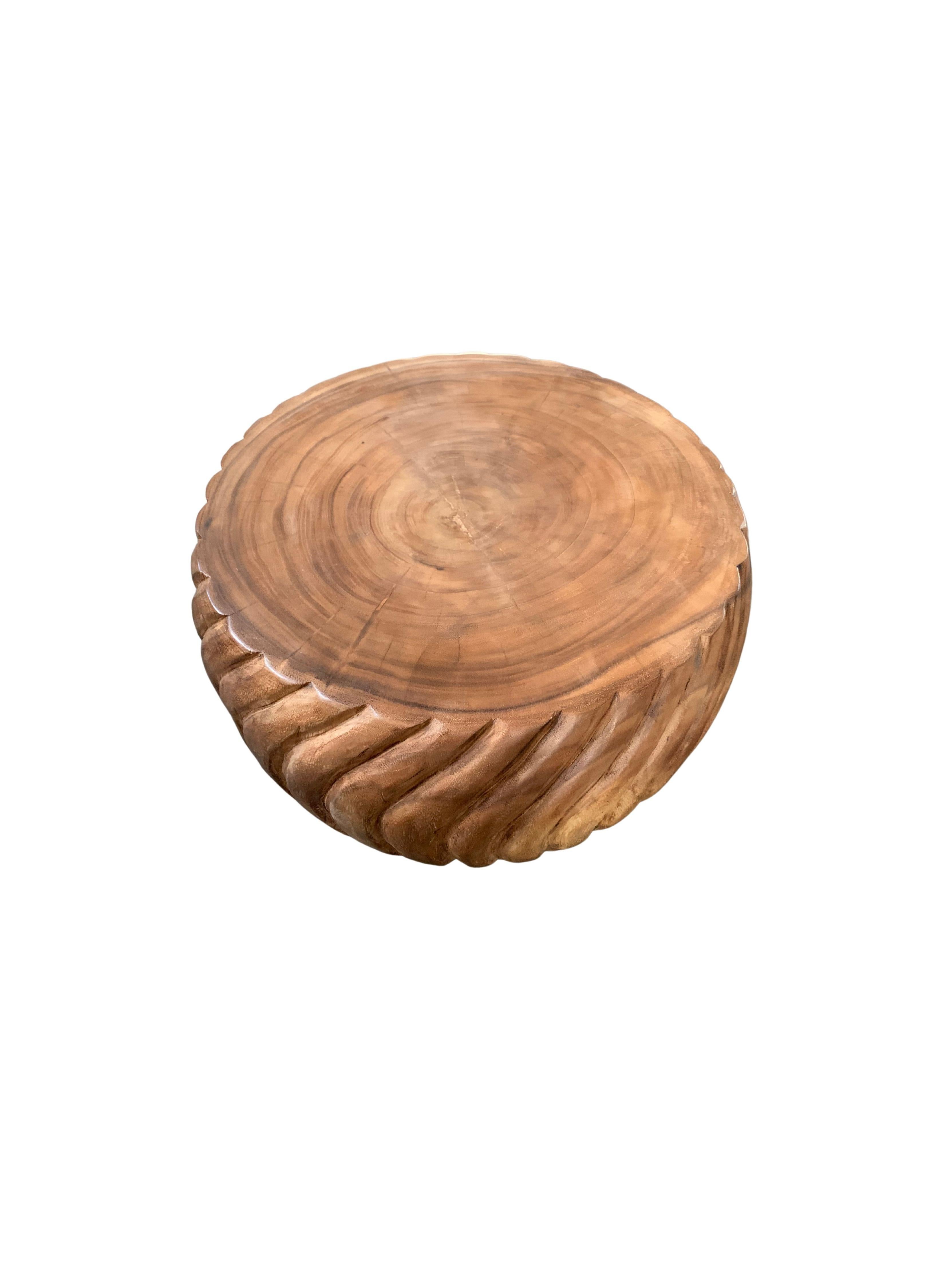 A wonderfully sculptural round side table with a hand-carved, ribbed design on its exterior. Its neutral pigment and subtle wood texture makes it perfect for any space. A uniquely sculptural and versatile piece certain to invoke conversation. This