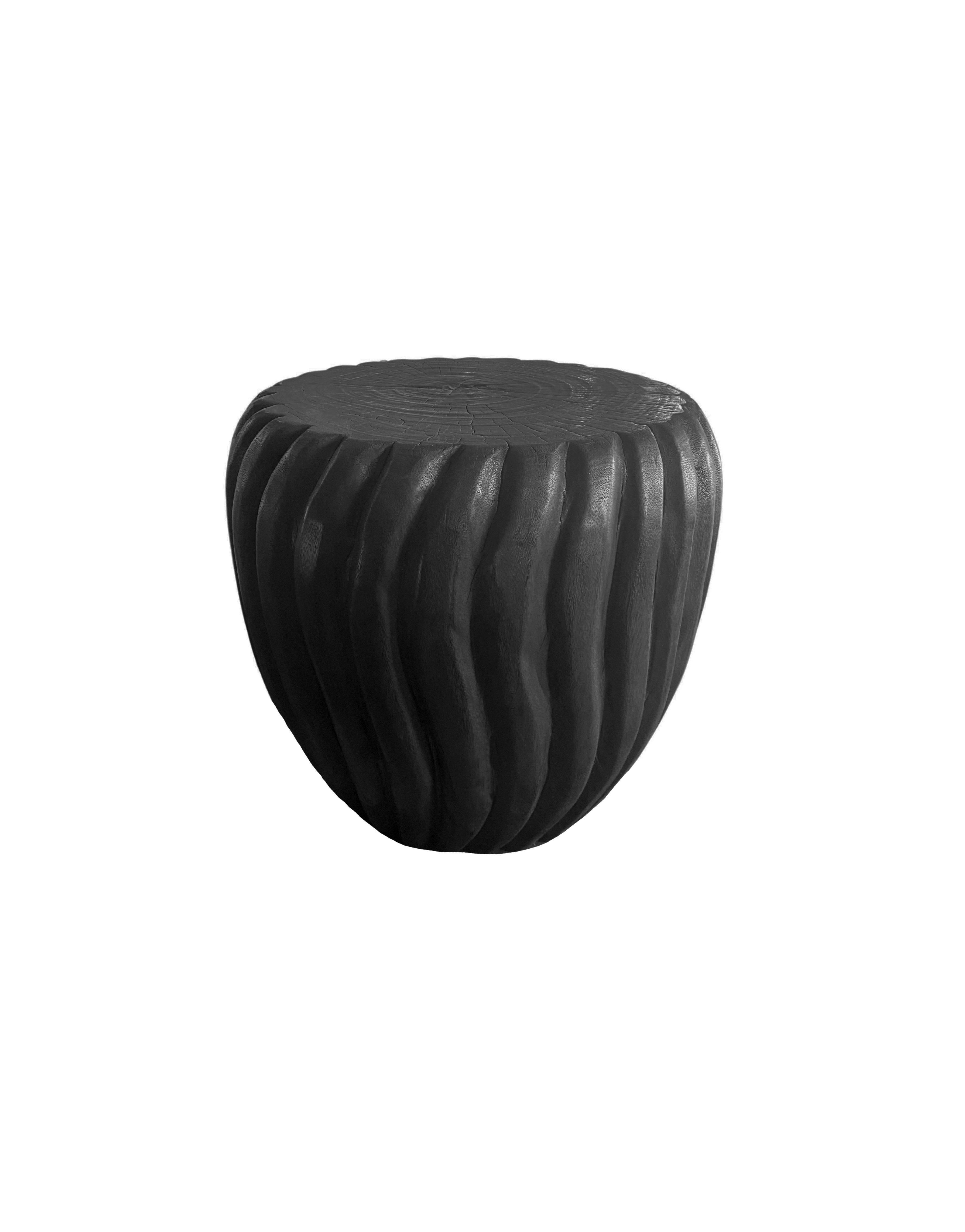 A wonderfully sculptural round side table with a hand-carved, ribbed design on its exterior. Its neutral pigment and subtle wood texture makes it perfect for any space. A uniquely sculptural and versatile piece certain to invoke conversation. This