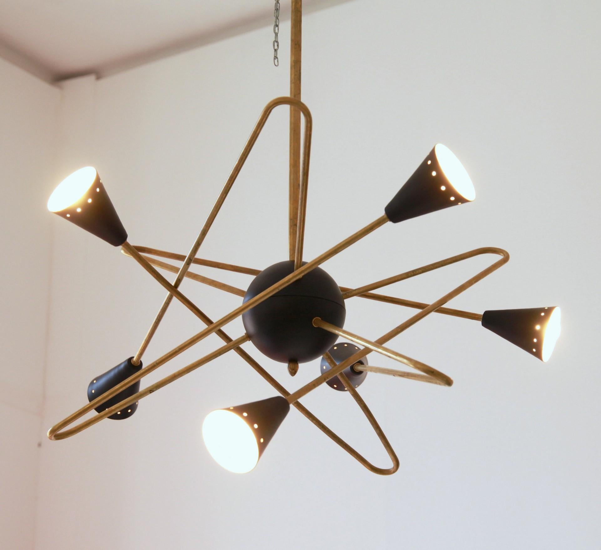 Midcentury six-arm design chandelier and patinated solid brass.
Each arm is curved.
Black shades at the end with the line of holes.

Use is for living room or corridor. Since each light beams laterally it gives ambience light and perfect for